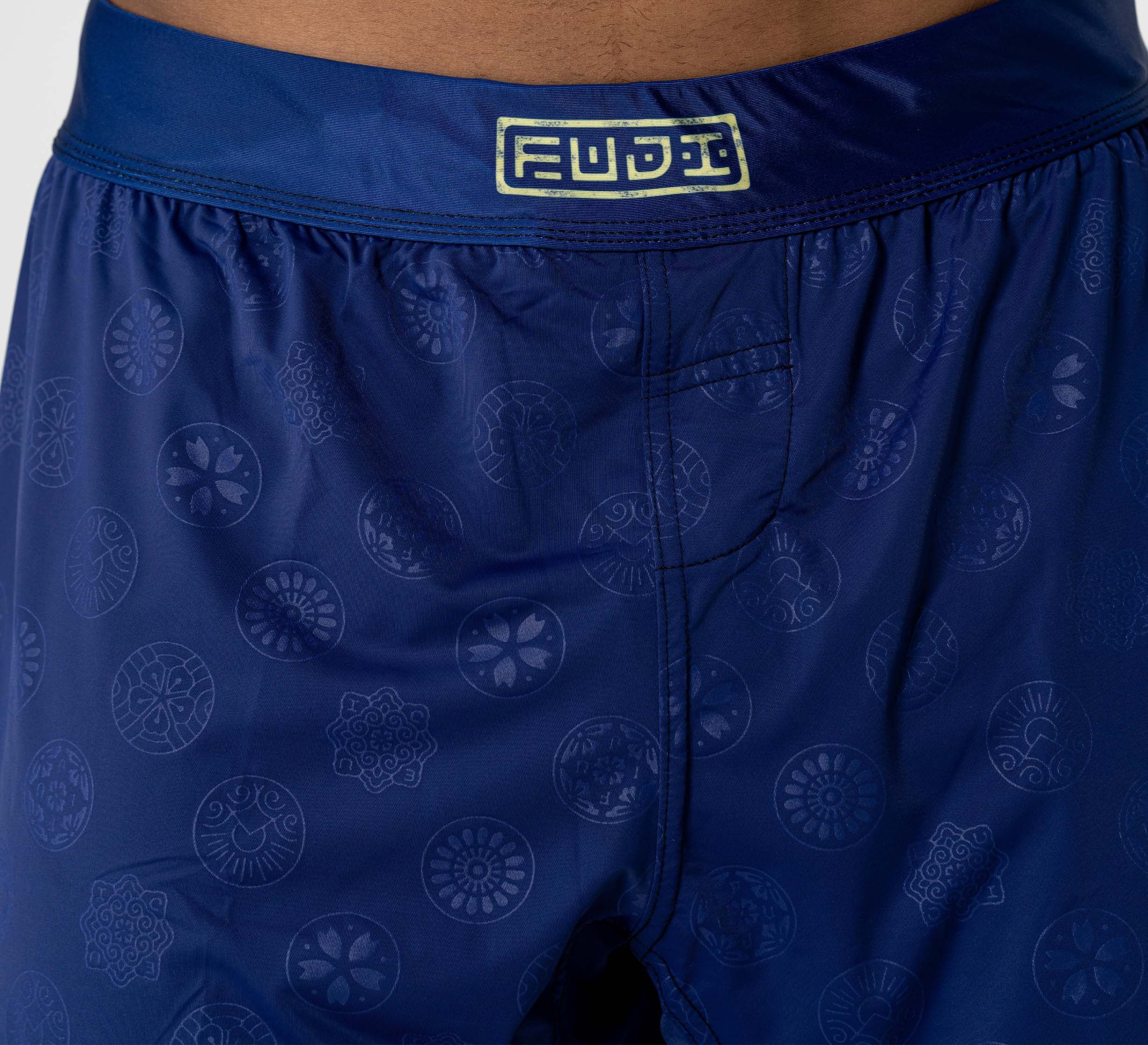 Close-up of a person wearing Shogun Heat Gear Shorts Navy, featuring a subtle circular pattern and a yellow FUJI logo on the waistband.