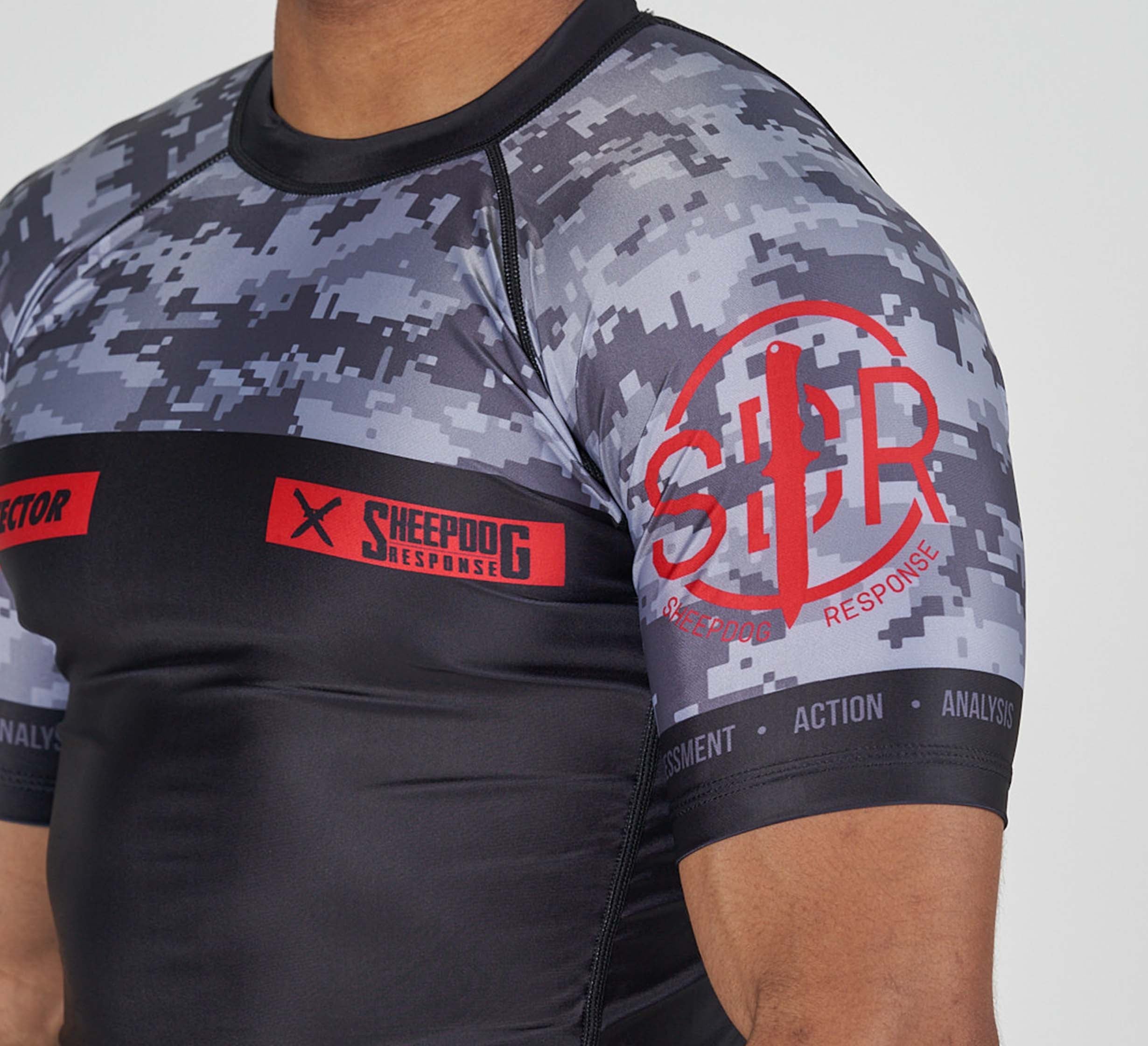 Someone is wearing the Sheepdog Response Flex Lite Rashguard Black, a fitted short-sleeve athletic shirt with a gray and black digital camo pattern and red Sheepdog Response logos on the sleeve and chest.