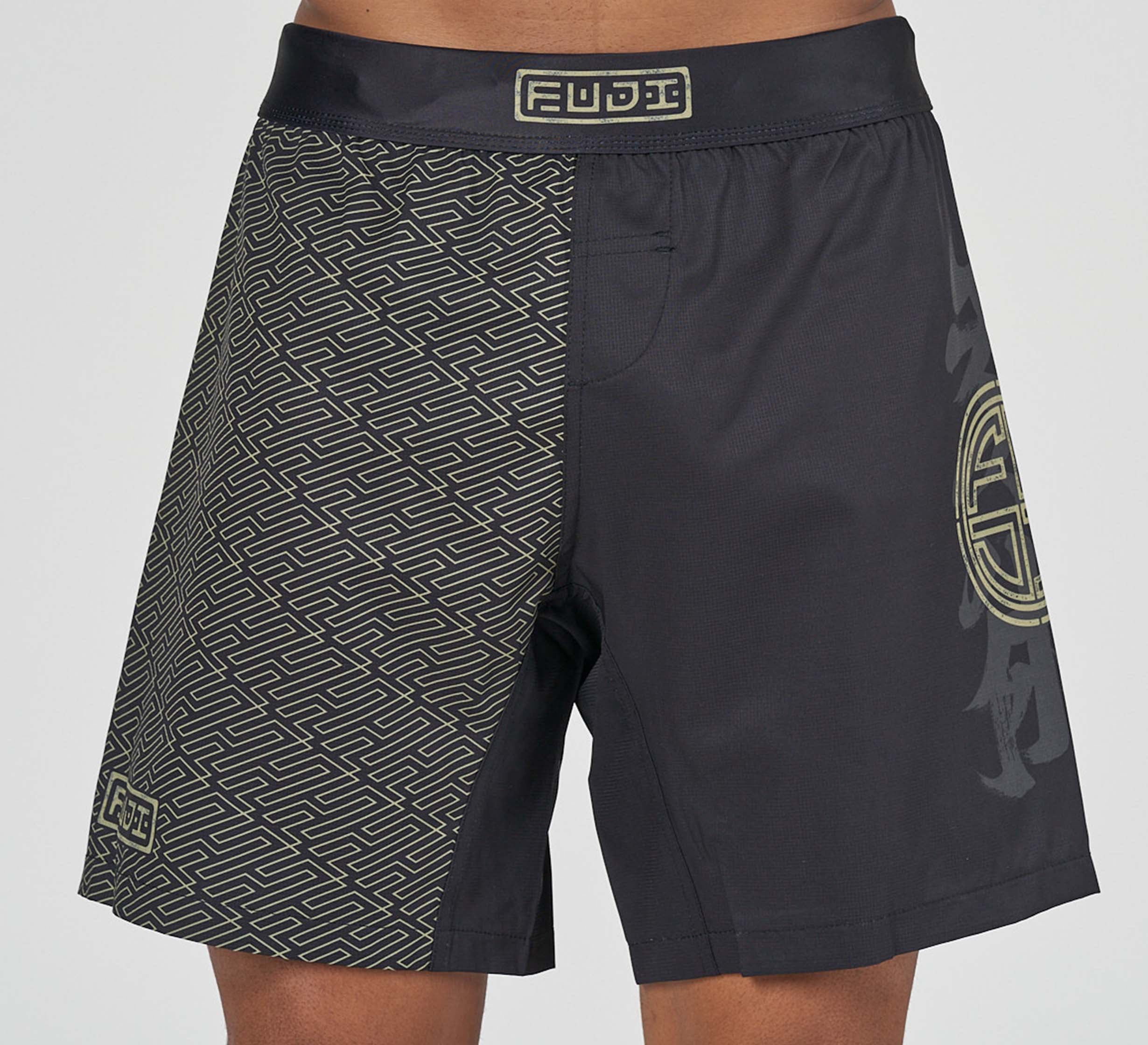 Bushido Flex Lite Shorts: black shorts with a geometric gold pattern on the left leg, a solid black right leg with a large circular symbol, and gold FUDJI logo patches on the waistband and lower left leg.