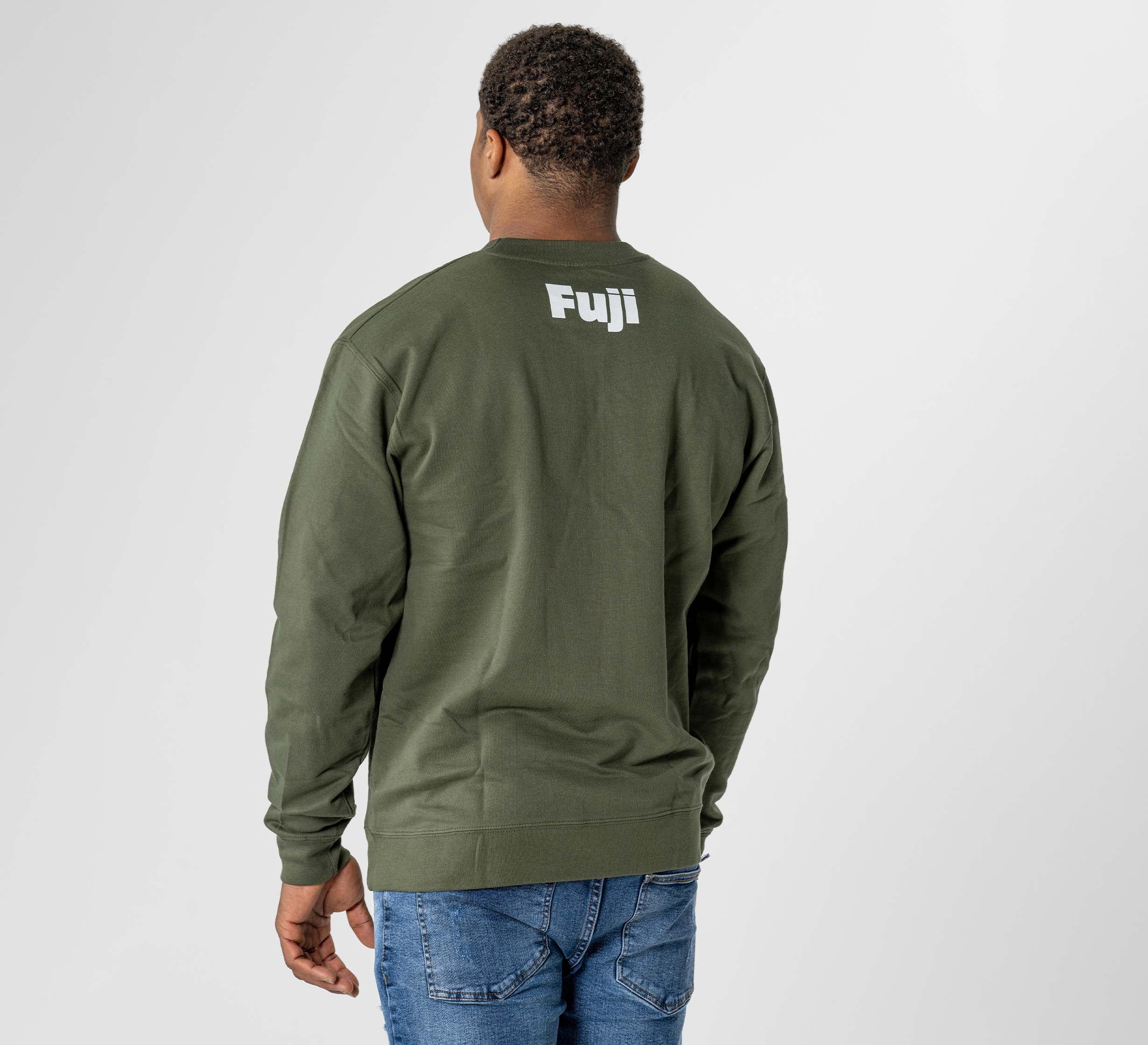 A person stands facing away in the Jiu Jitsu Player Crewneck Military Green, featuring "Fuji" printed in white on the back, paired with blue jeans against a plain light background.