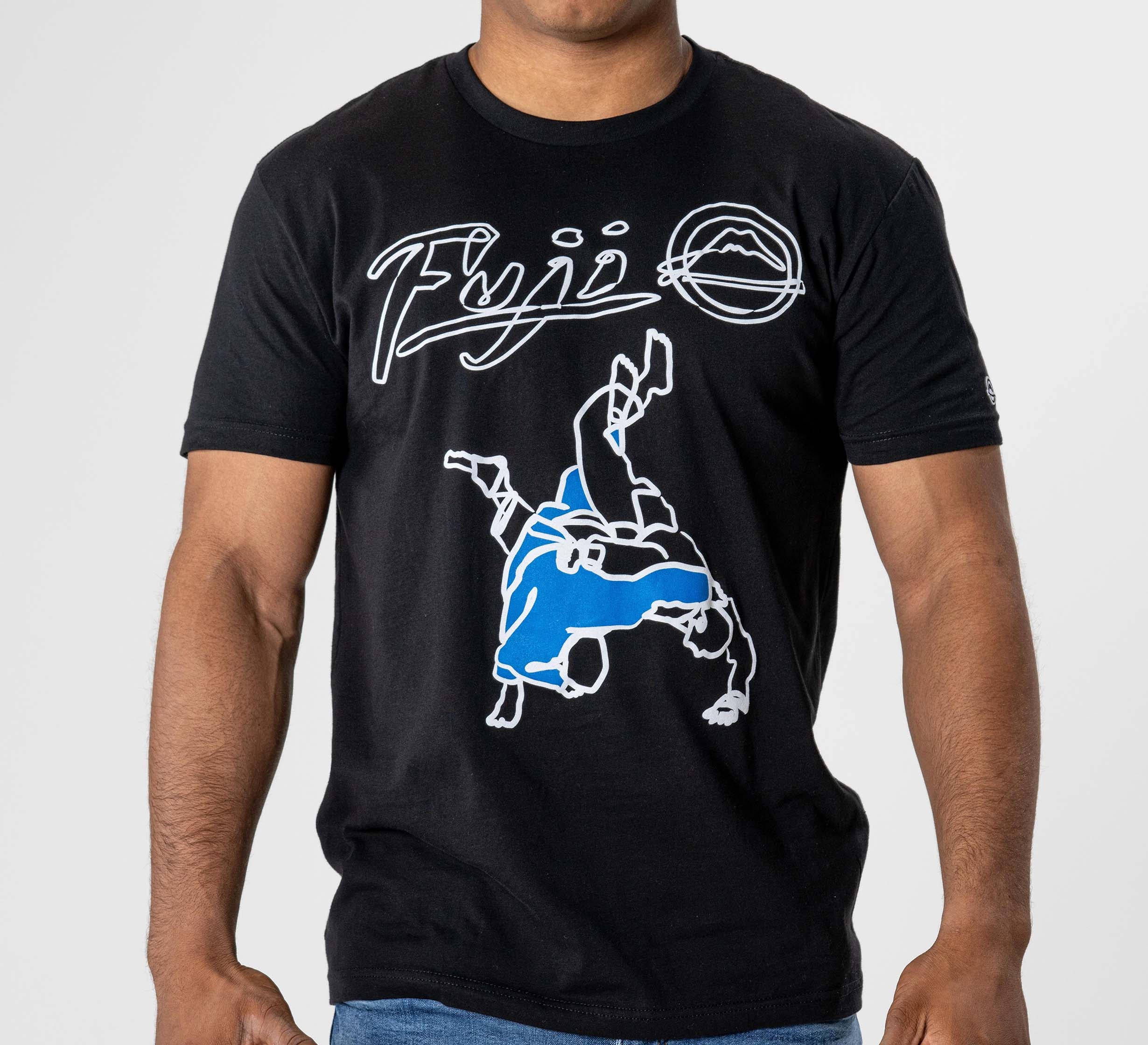 A person wears the FUJI Takedown T-Shirt Black, featuring stylized "Fuji" text, a graphic of two judo figures (one in blue executing a throw), and a small mountain logo.
