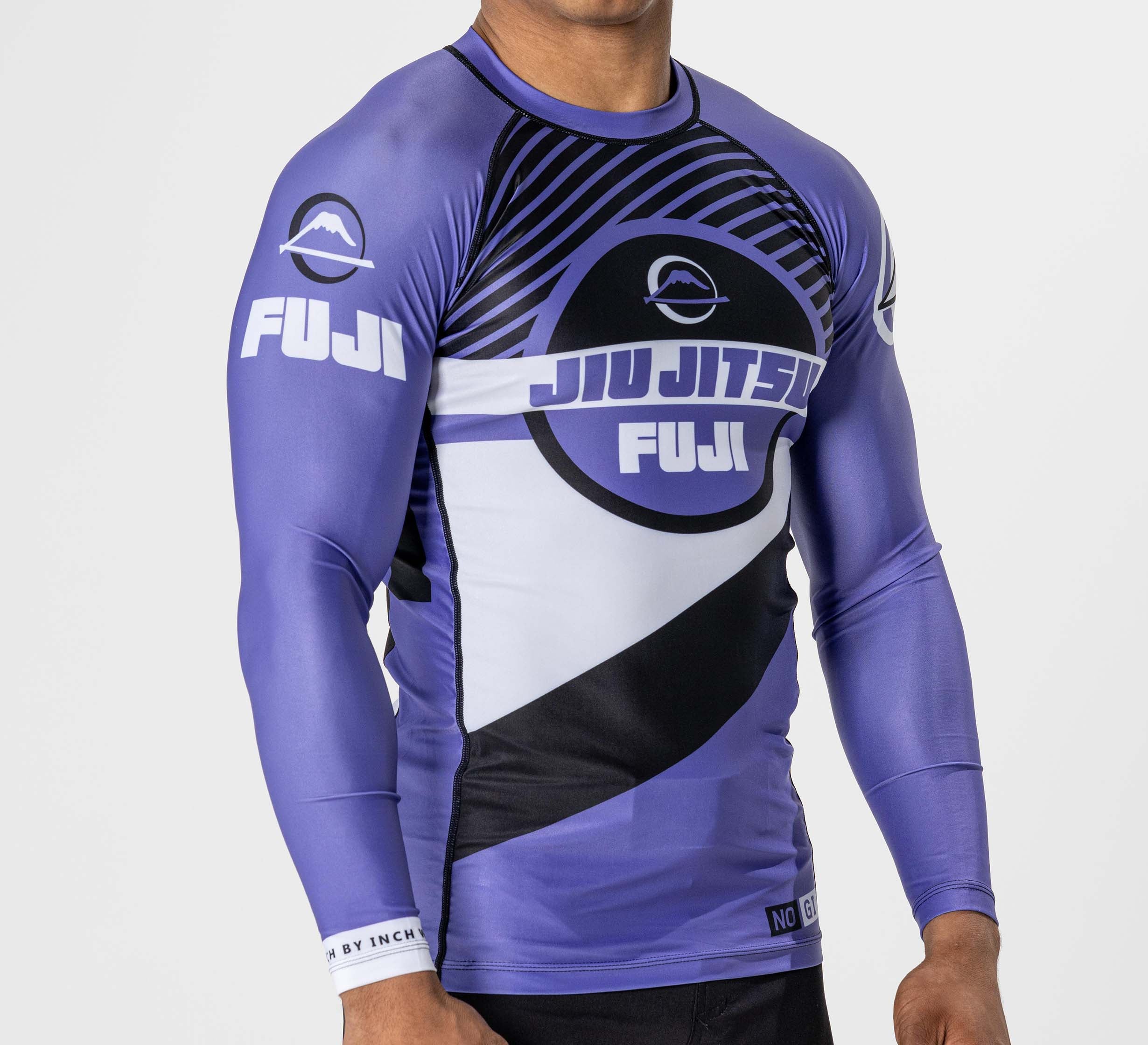 A person wearing the Pacer Flex Lite Long Sleeve Rashguard Purple, featuring bold white and black geometric patterns and the FUJI logo on the chest and sleeves, stands against a plain white background.