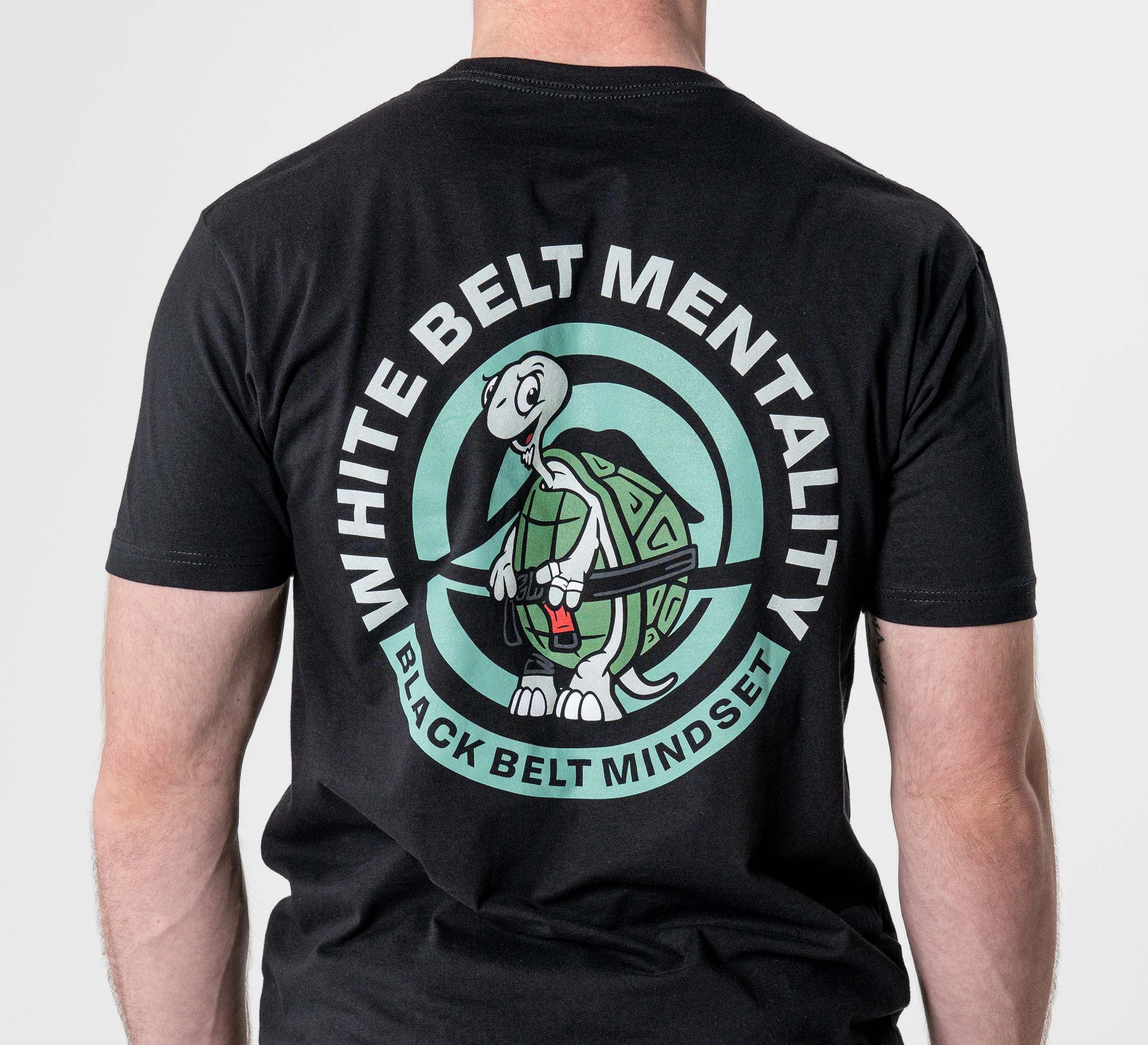 Someone wears the Black Belt Mentality T-Shirt Black, featuring a cartoon turtle with a red belt and the phrases "WHITE BELT MENTALITY" and "BLACK BELT MINDSET" around it.