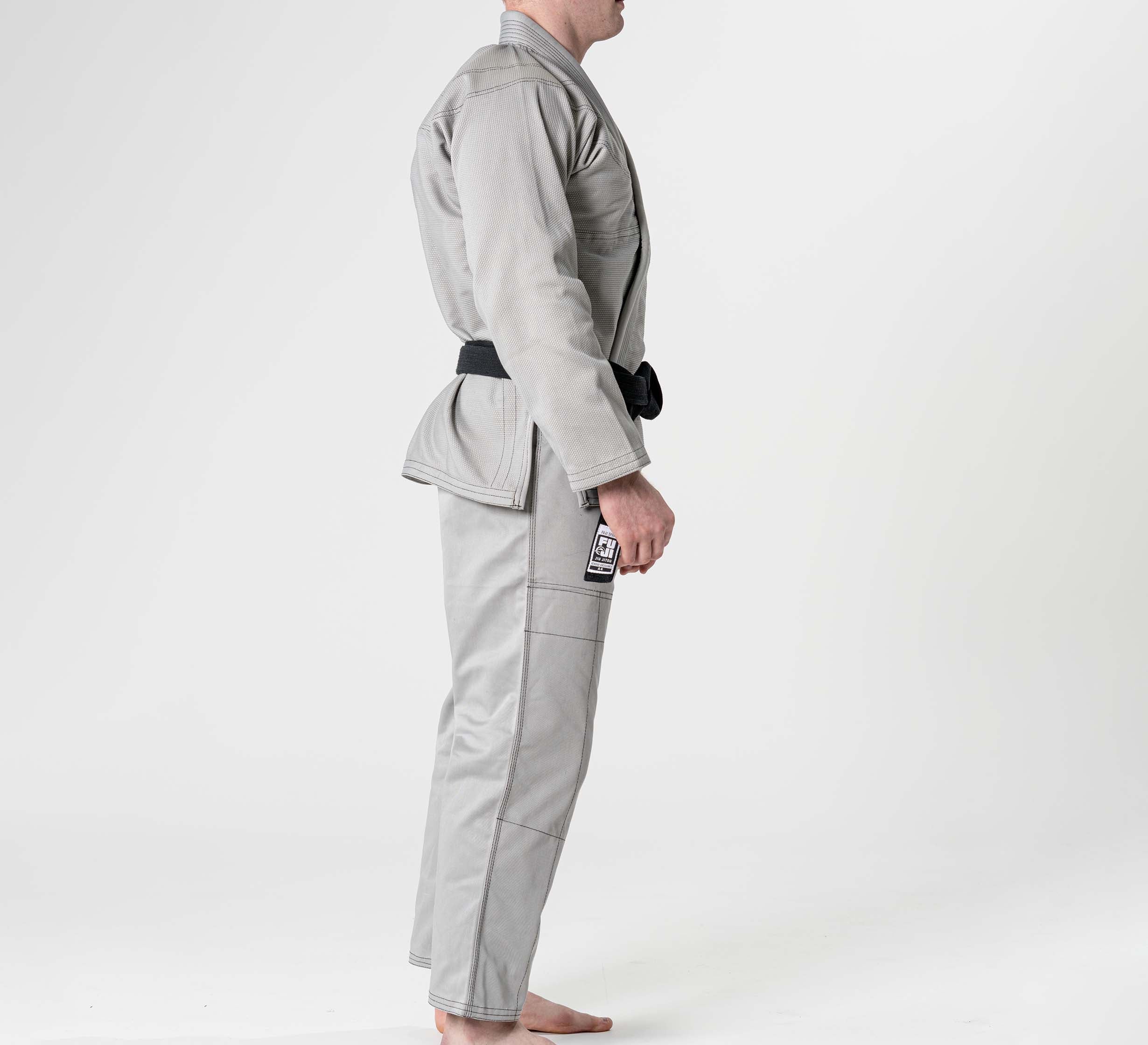 A person stands barefoot in profile, wearing the Lightweight BJJ Gi Grey with a black belt, set against a plain white background.