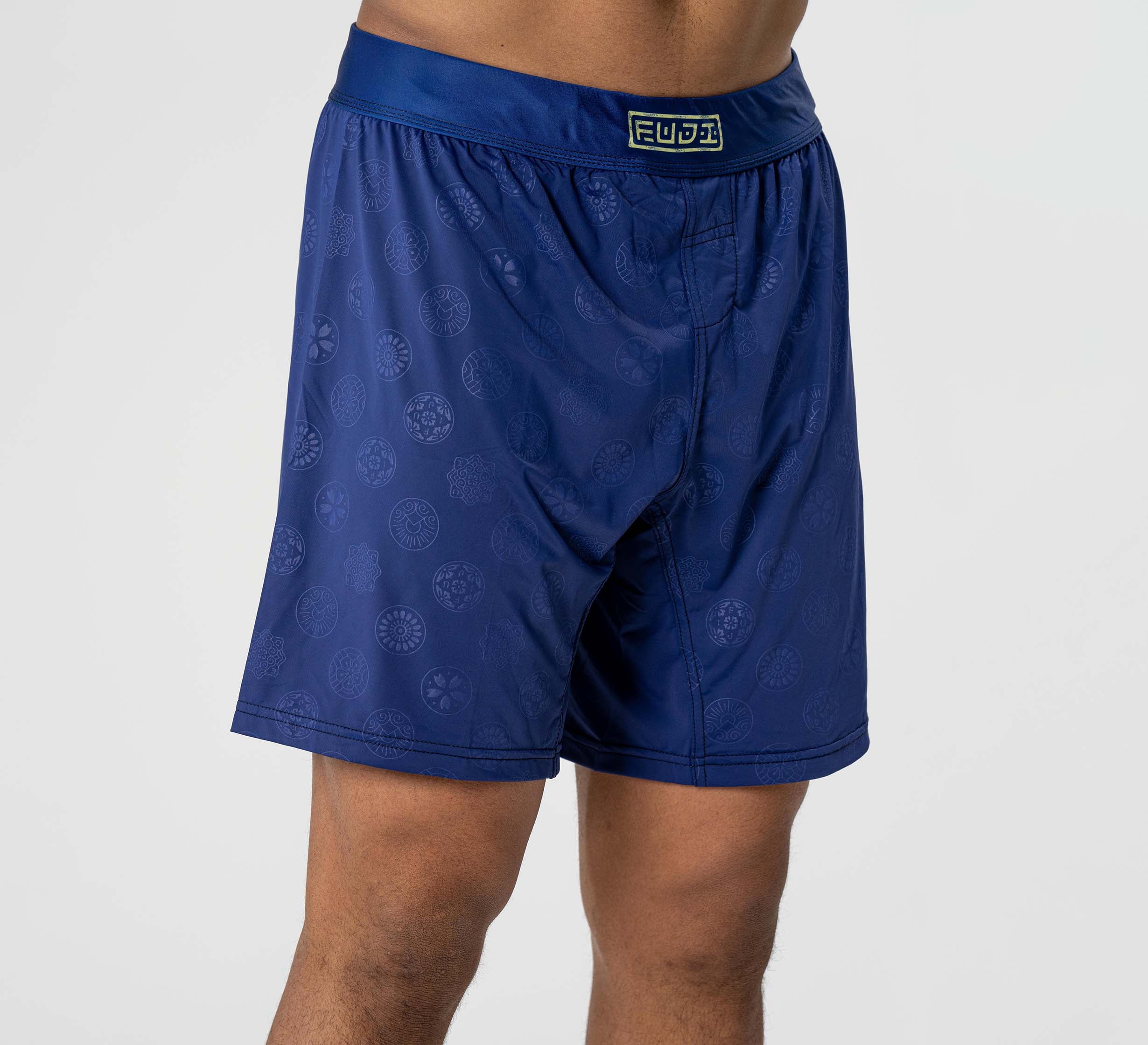 A person wearing Shogun Heat Gear Shorts Navy with subtle circular patterns and a FUJI logo on the waistband, standing against a plain light background.
