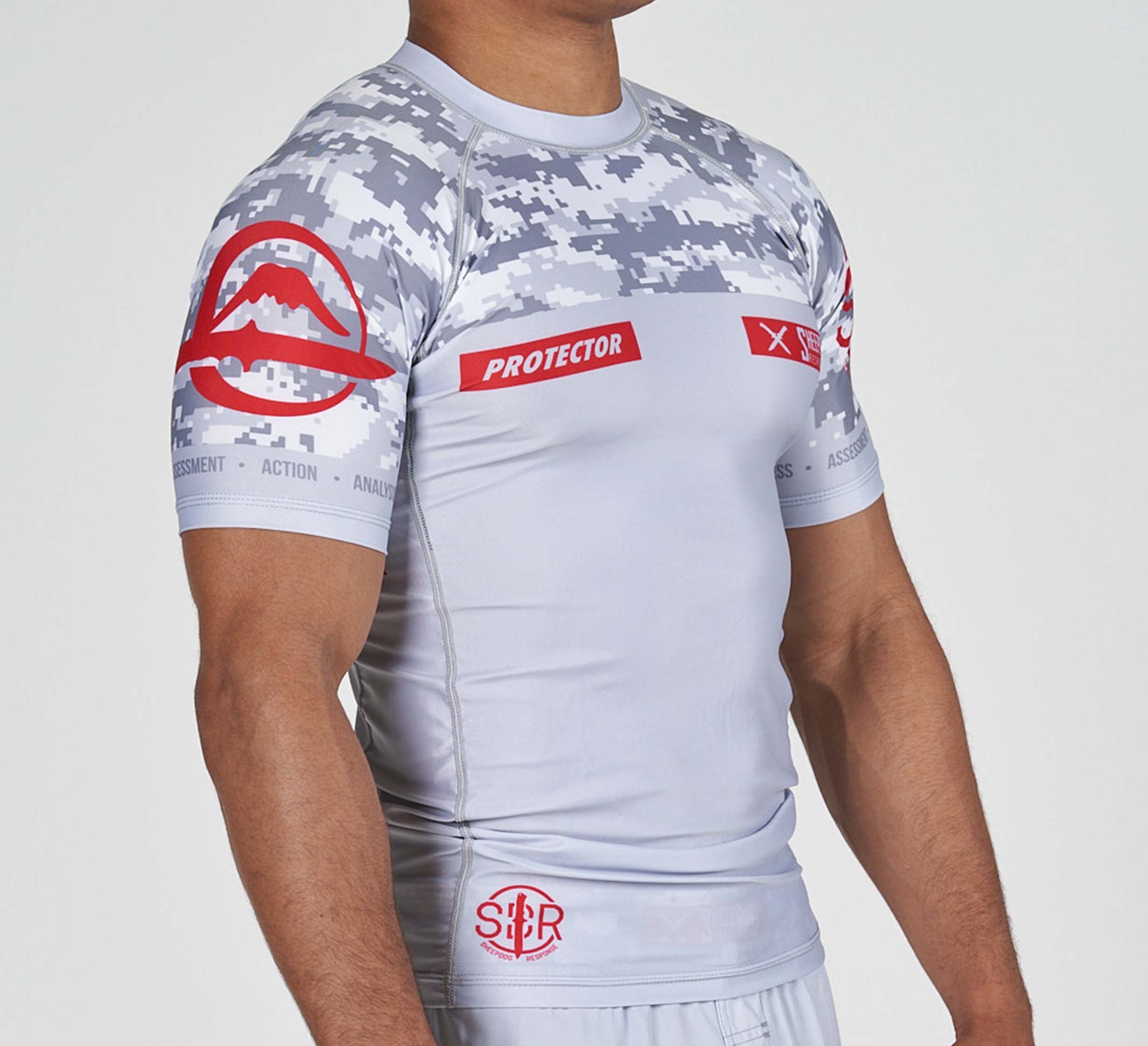 A person wearing the Sheepdog Response Flex Lite Rashguard Grey, a fitted short-sleeve shirt with gray digital camo, red logos, and "PROTECTOR" on the chest, photographed from the side.