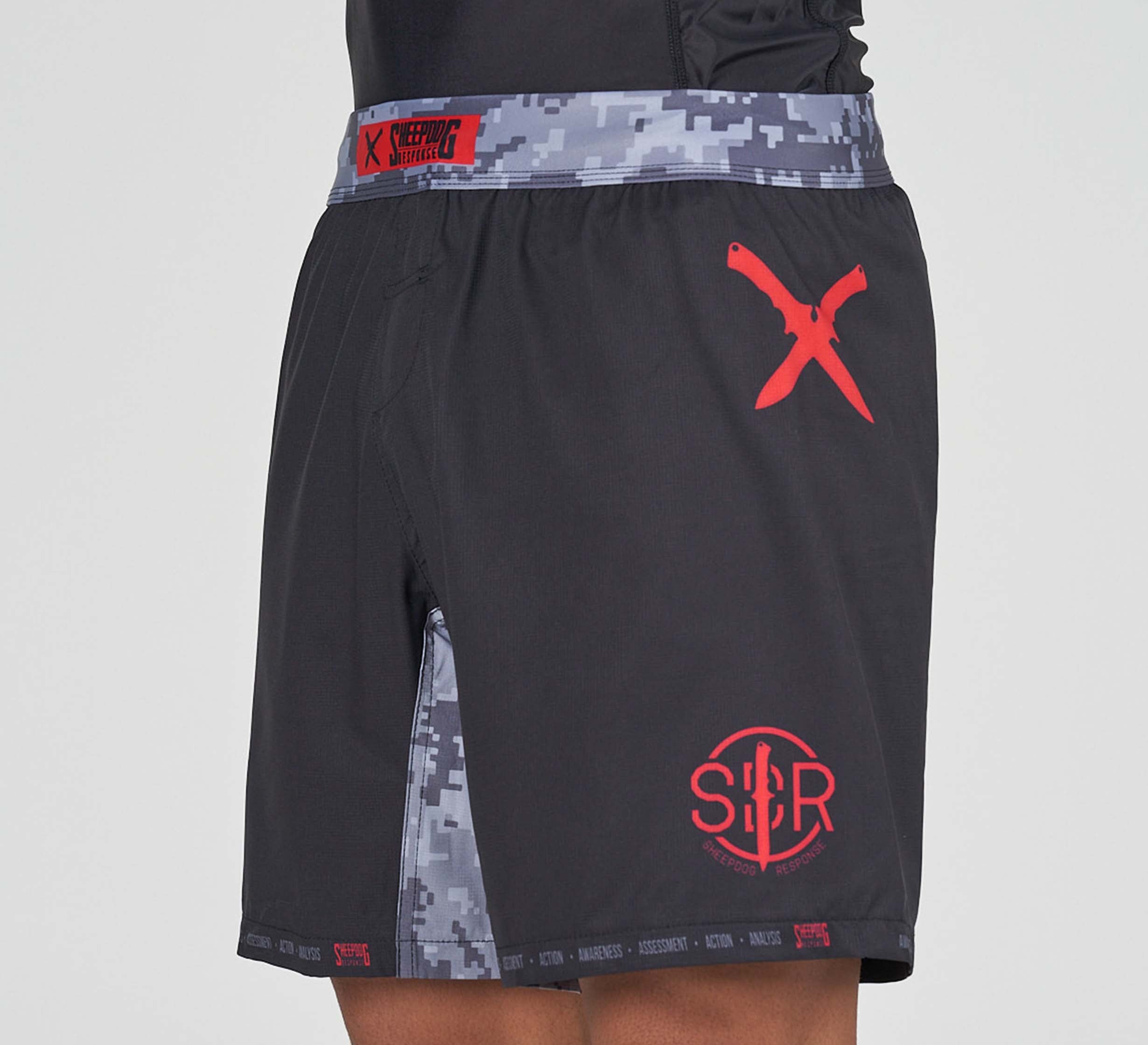 Someone wearing Sheepdog Response Flex Lite Shorts Black, which feature a red X and circular S/R logo, plus digital camouflage pattern on the sides and waistband.