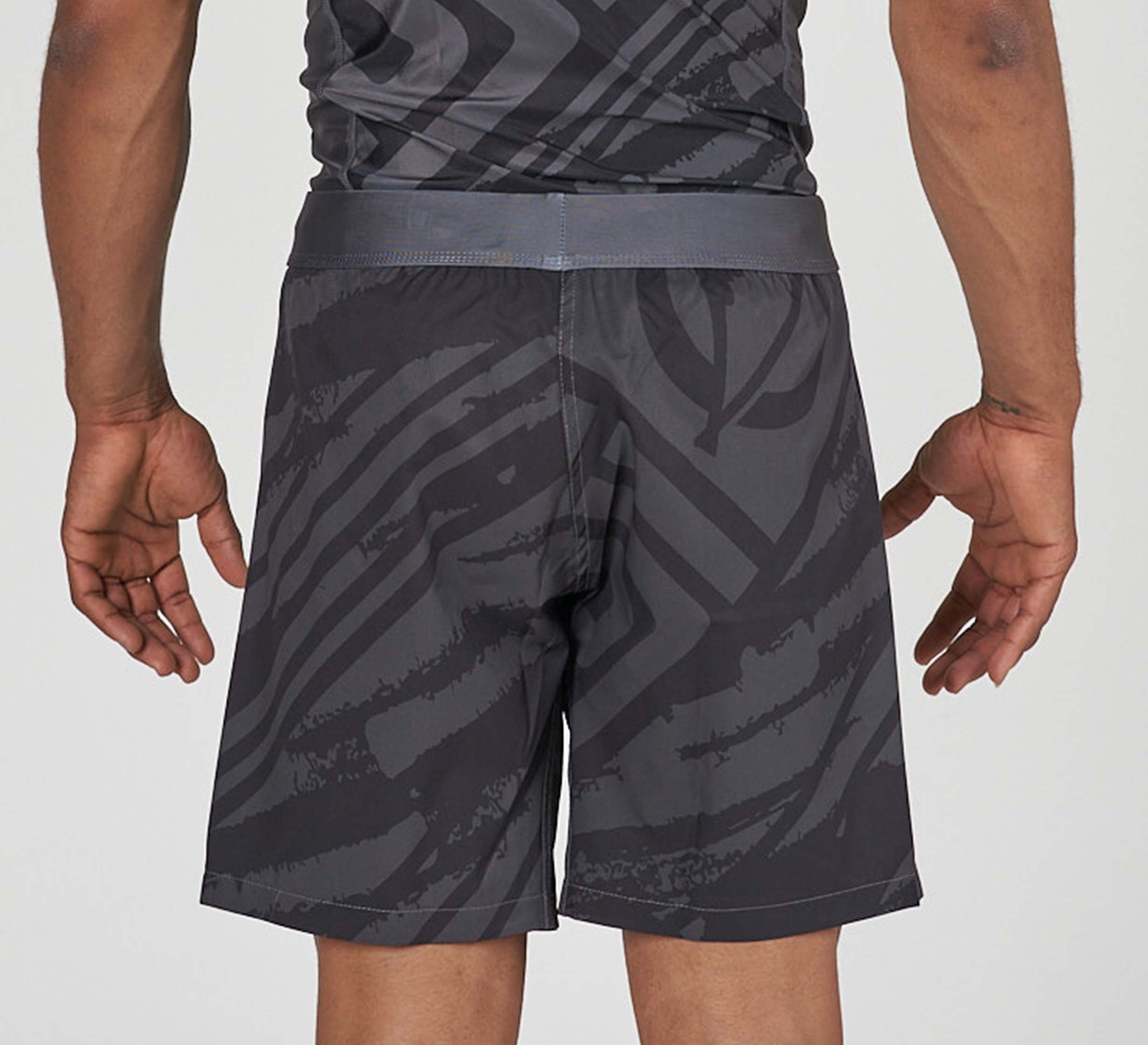 A person is seen from the back wearing Battle Flex Lite Shorts Black, featuring a dark gray abstract pattern, with their arms relaxed at their sides.