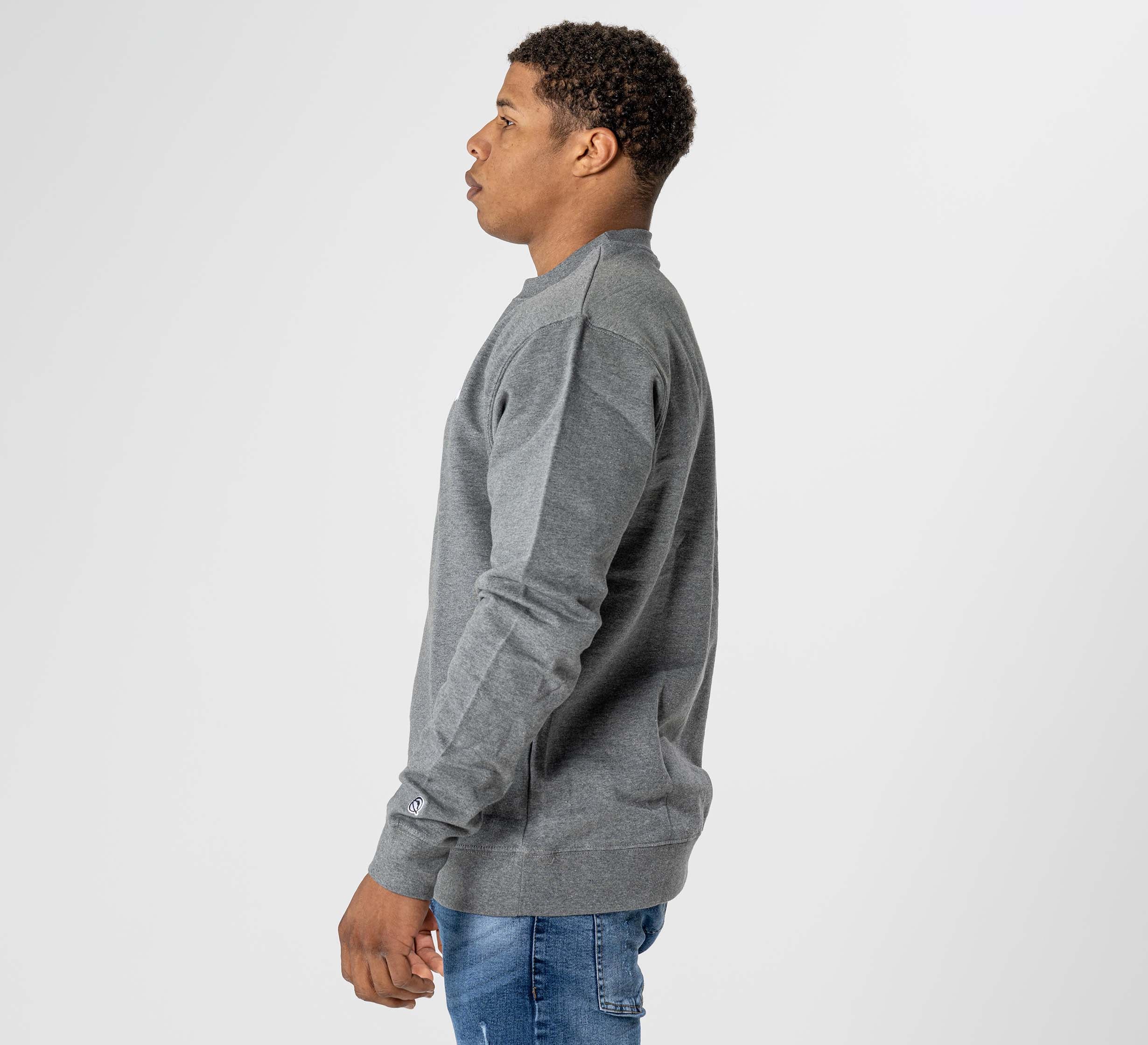 A man wearing the Jiu Jitsu Player Crewneck Heather Grey and blue jeans stands in profile against a plain white background.