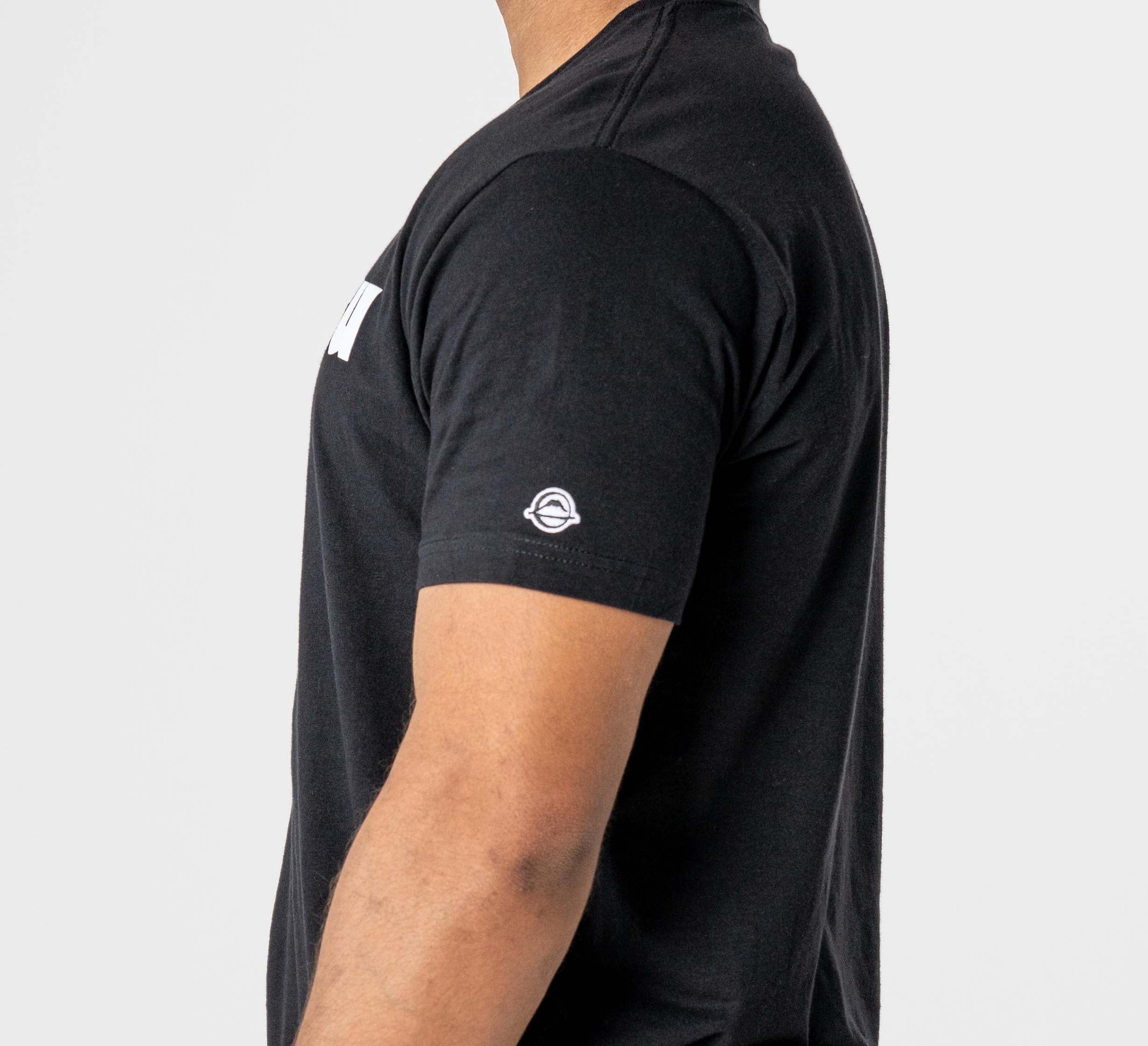 A person wearing the Jiu Jitsu Player T-Shirt Black, featuring a small white circular logo on the left sleeve, is shown from the side against a plain white background.