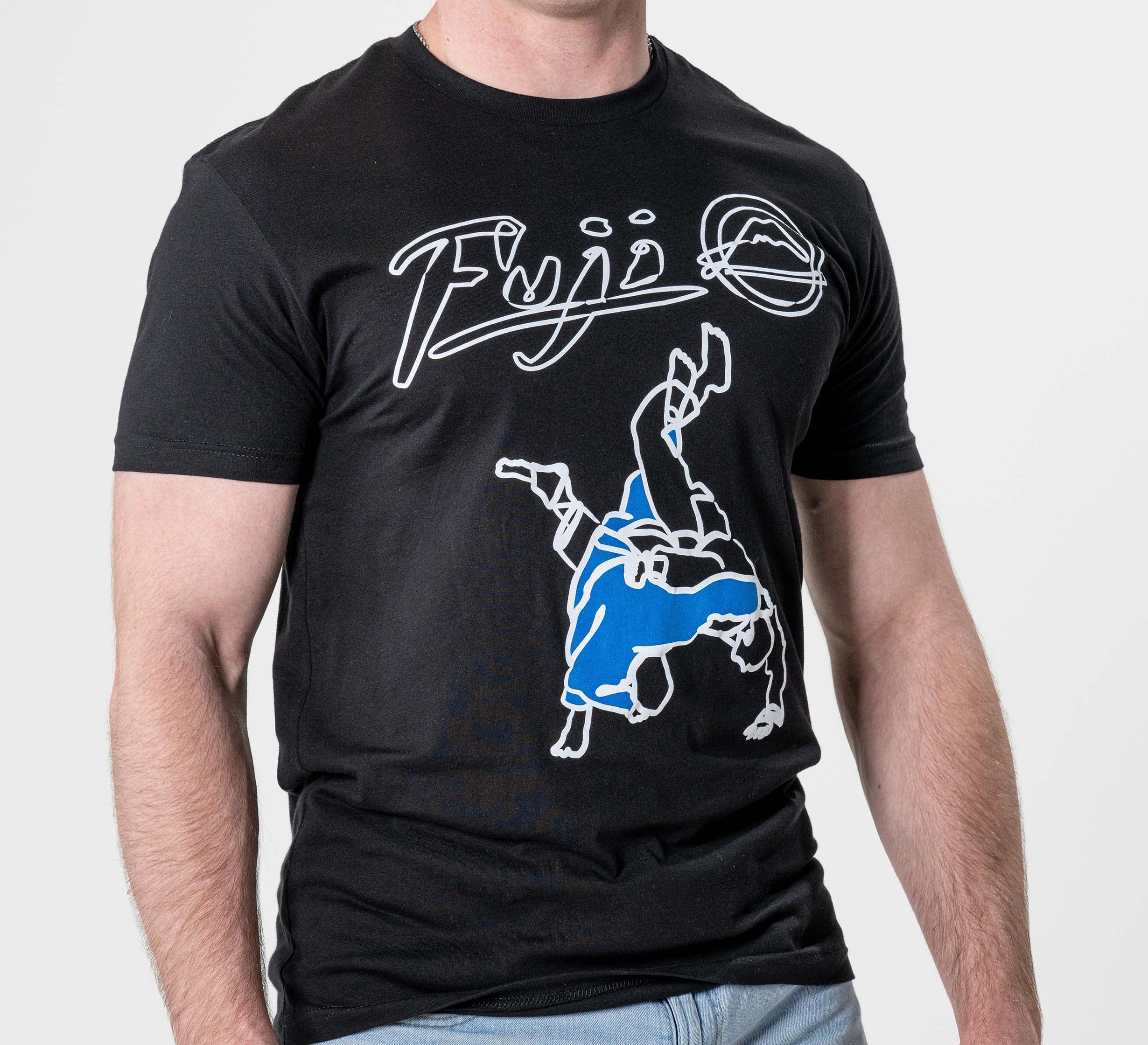A person wearing the FUJI Takedown T-Shirt Black, featuring "Fuji" and a mountain logo above two figures practicing a martial arts throw, with one figure in blue.