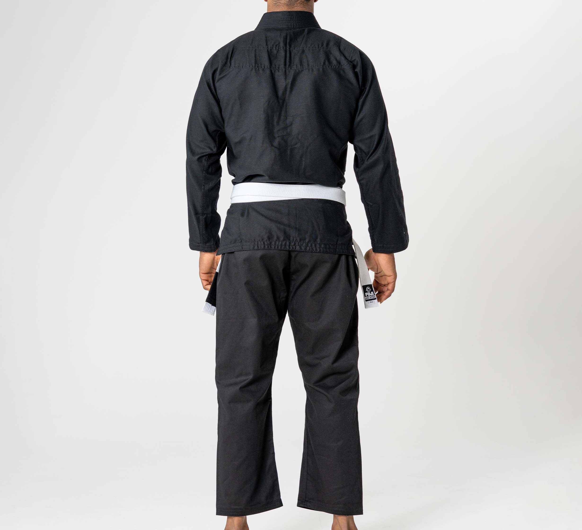 A person stands barefoot, facing away from the camera, wearing the Starter Adult BJJ Gi Black with a white belt against a plain white background.