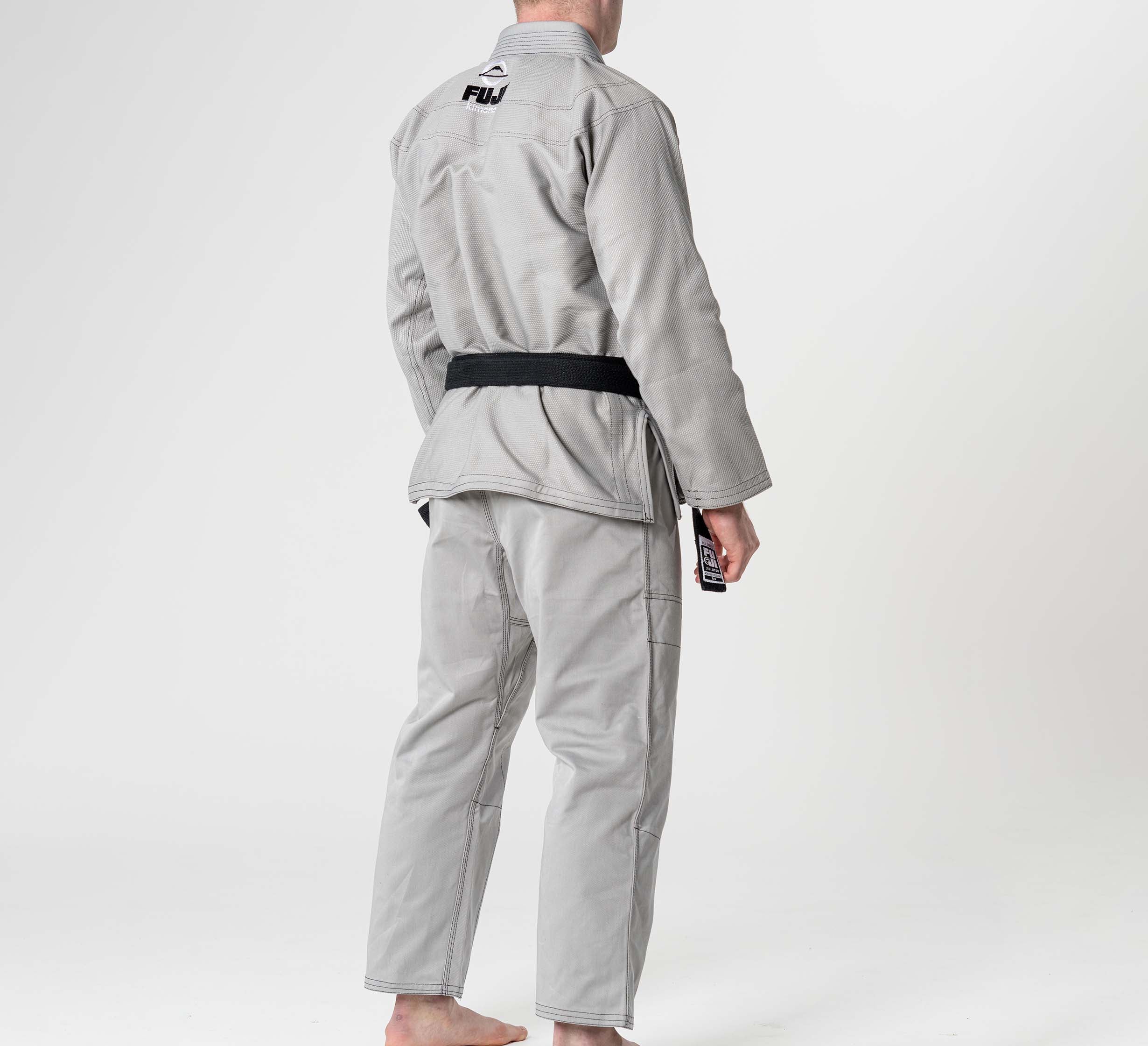 A person wearing the Lightweight BJJ Gi Grey with a black belt stands barefoot, facing away from the camera on a plain white background.