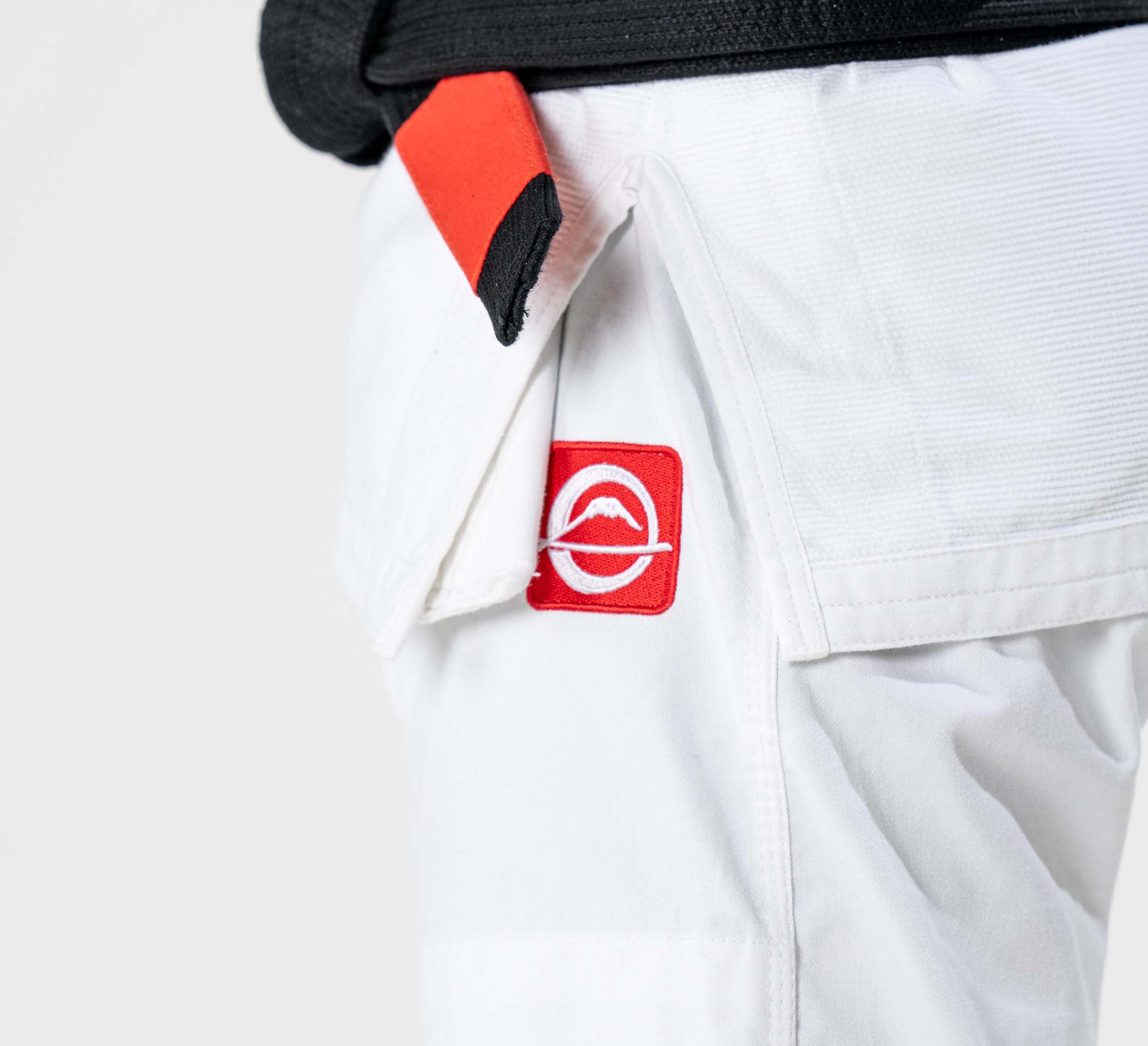 Close-up of a person wearing the Ultra Lite 300 BJJ Gi White, featuring a red and white patch on the pants and a black belt with red bar, set against a plain light background.