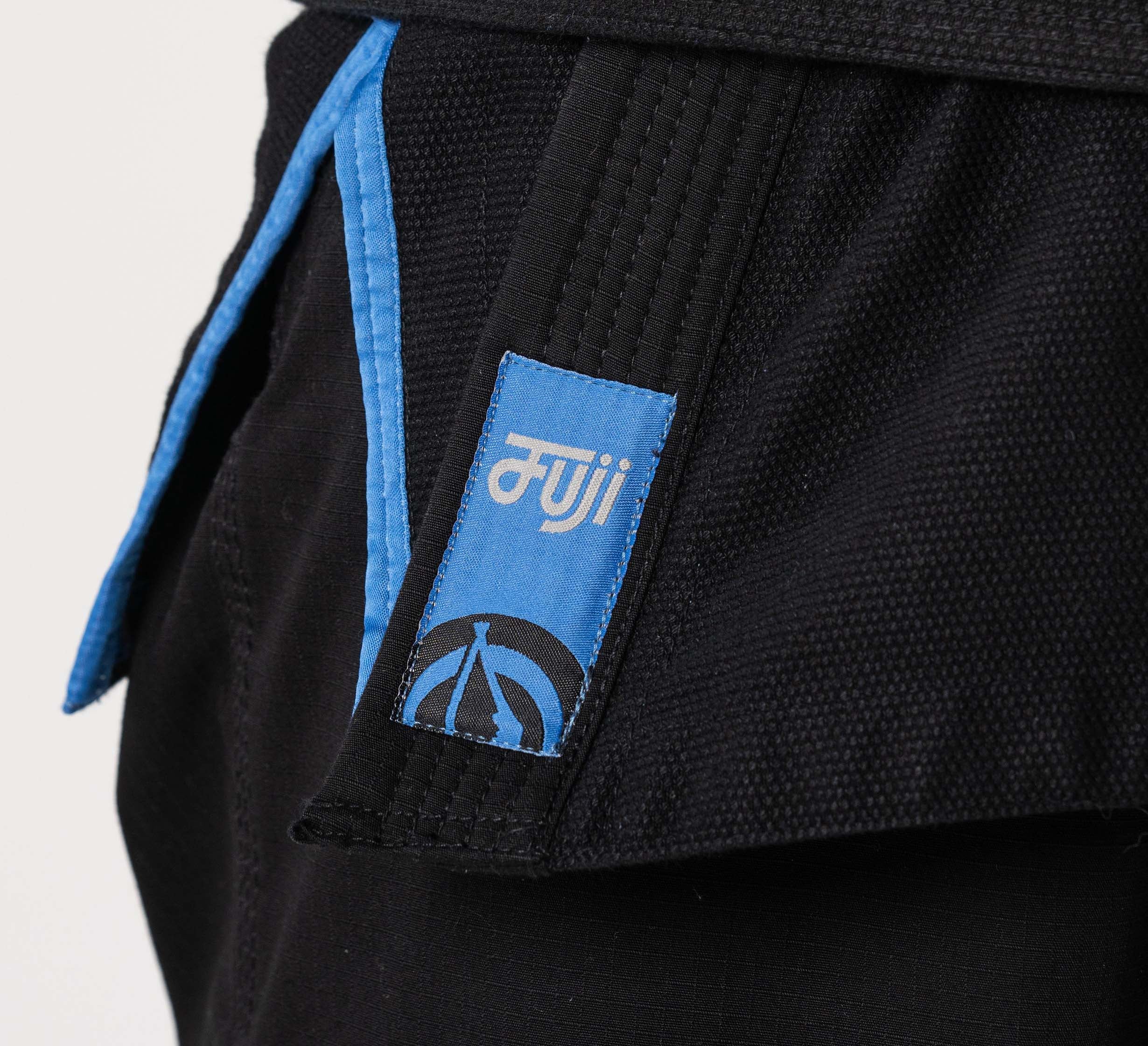 Close-up of the Flow-Tech BJJ Gi in black with blue trim and a blue patch featuring white text and a circular symbol on the side of the pants.