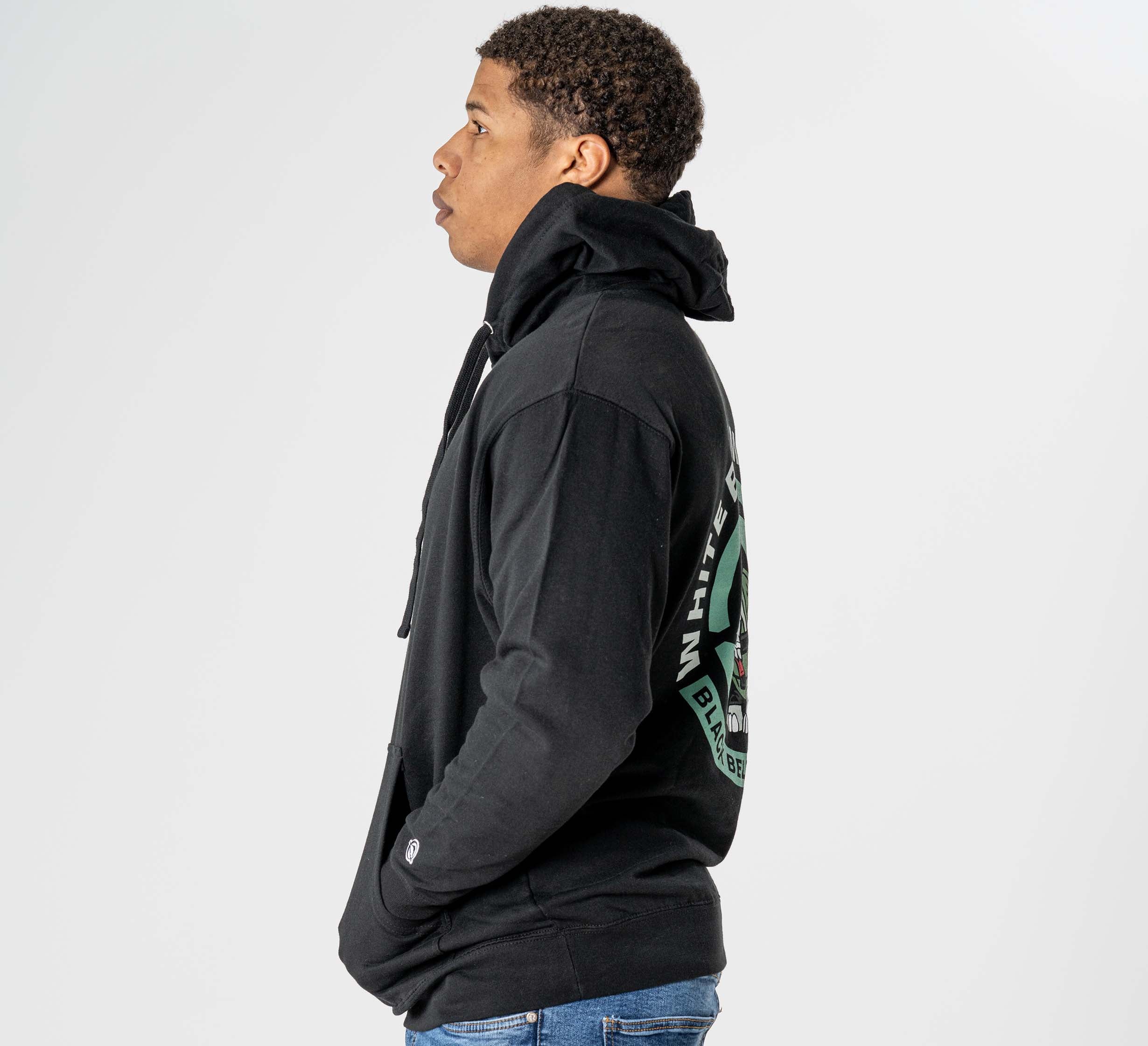 A person in profile wears the Black Belt Mentality Hoodie Black, featuring a large hood and graphic back design, paired with blue jeans against a plain white background.