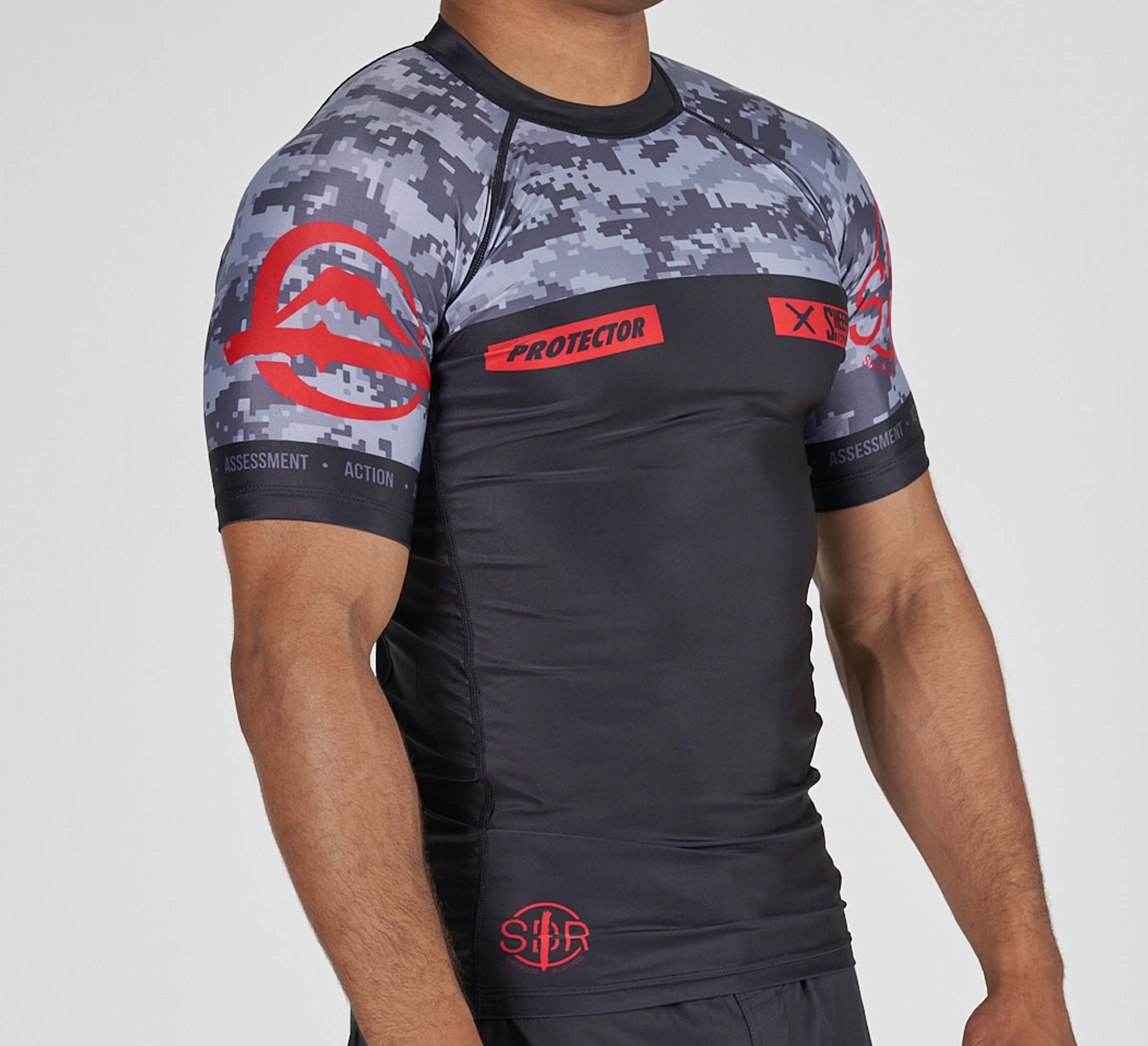 A person wears the Sheepdog Response Flex Lite Rashguard in black, featuring a fitted black and gray camo pattern with red accents, "PROTECTOR" text, and symbols on the chest and sleeves. Only the upper body and arms are shown.