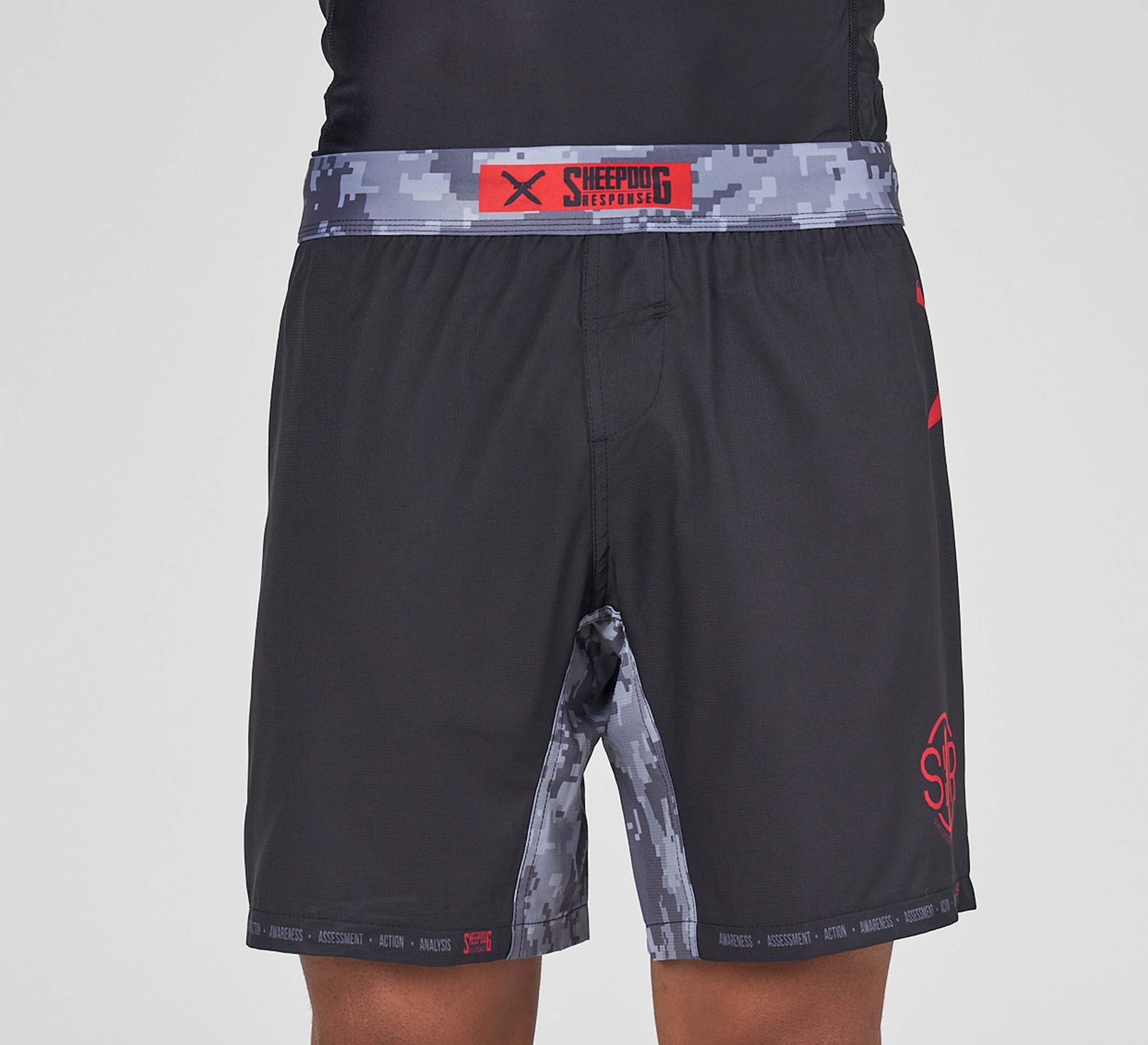 A person wearing Sheepdog Response Flex Lite Shorts Black, featuring a gray digital camo waistband and side panels, red logo, and "SHEEPDOG RESPONSE" on the waistband. The upper body is partially visible.