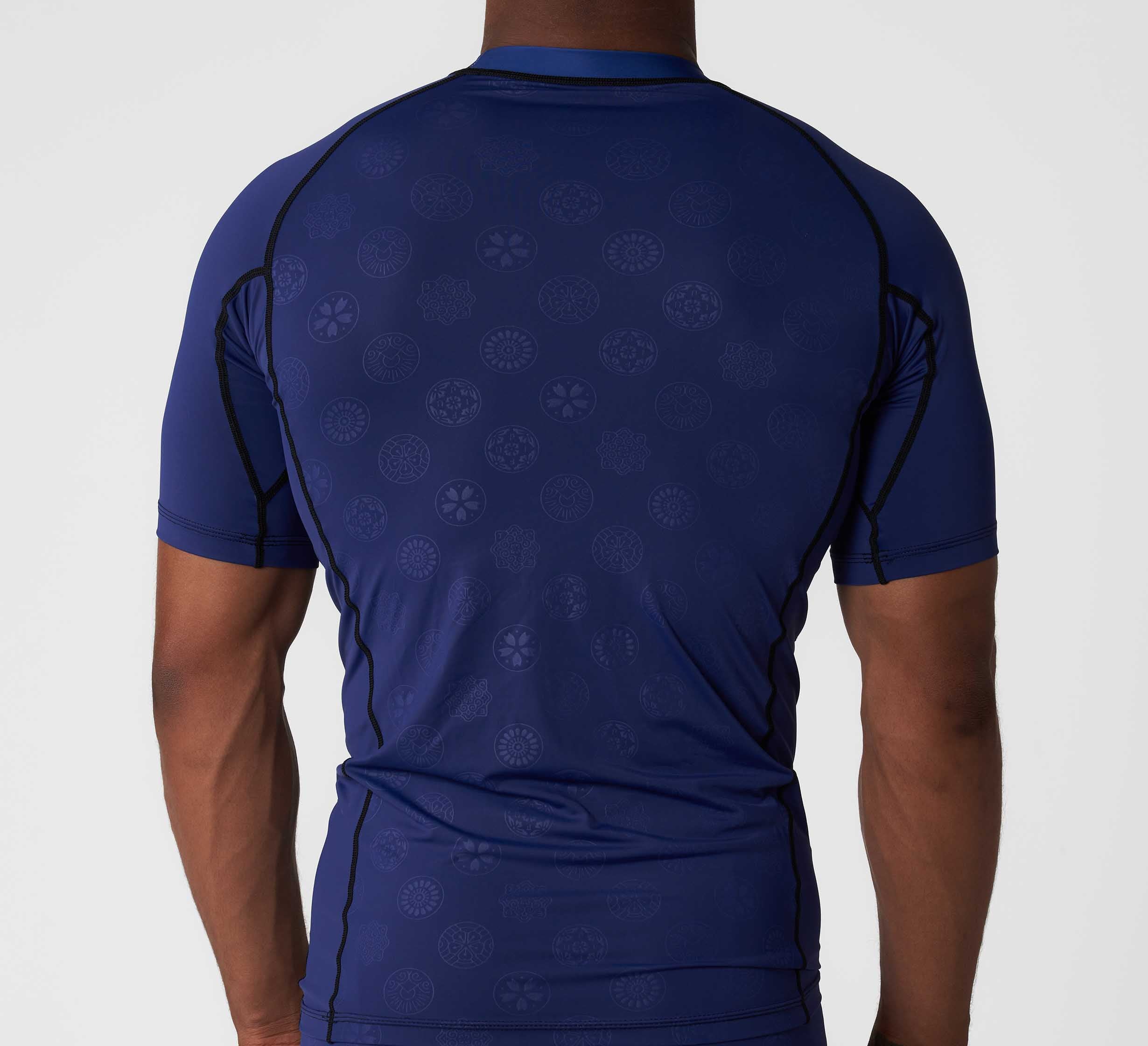 A person wearing the Shogun Heat Gear Rashguard Navy, a fitted short-sleeve athletic shirt with subtle circular patterns, shown from the back against a plain white background.