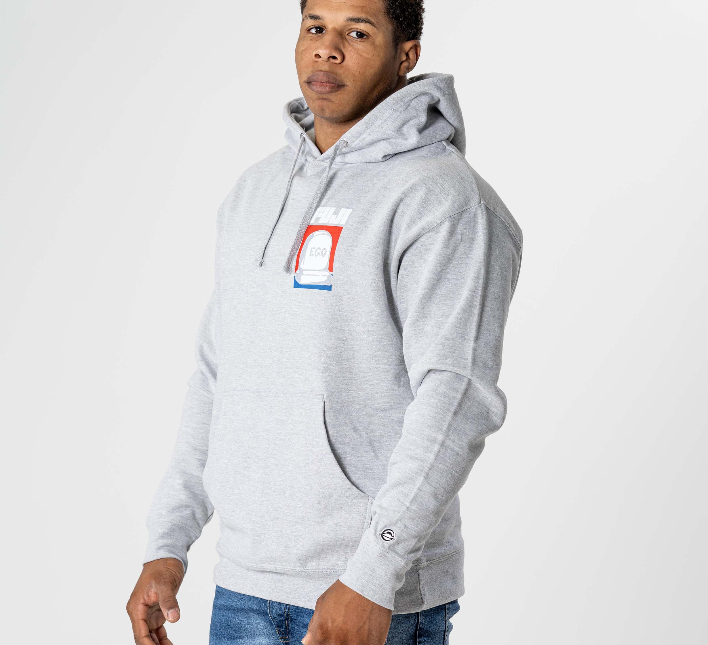 A man wearing the Submit Your Ego Hoodie Heather Grey, featuring a colorful rectangular logo on the chest and paired with blue jeans, stands against a plain white background looking slightly to the side.