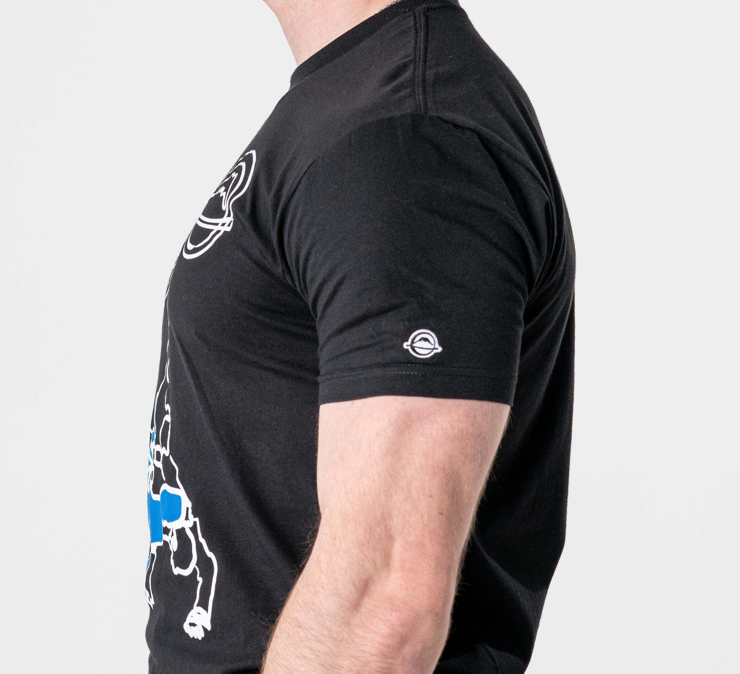 A person is shown from the side against a plain light background, wearing the FUJI Takedown T-Shirt Black, which features a white chest graphic and a small white circular logo on the sleeve.