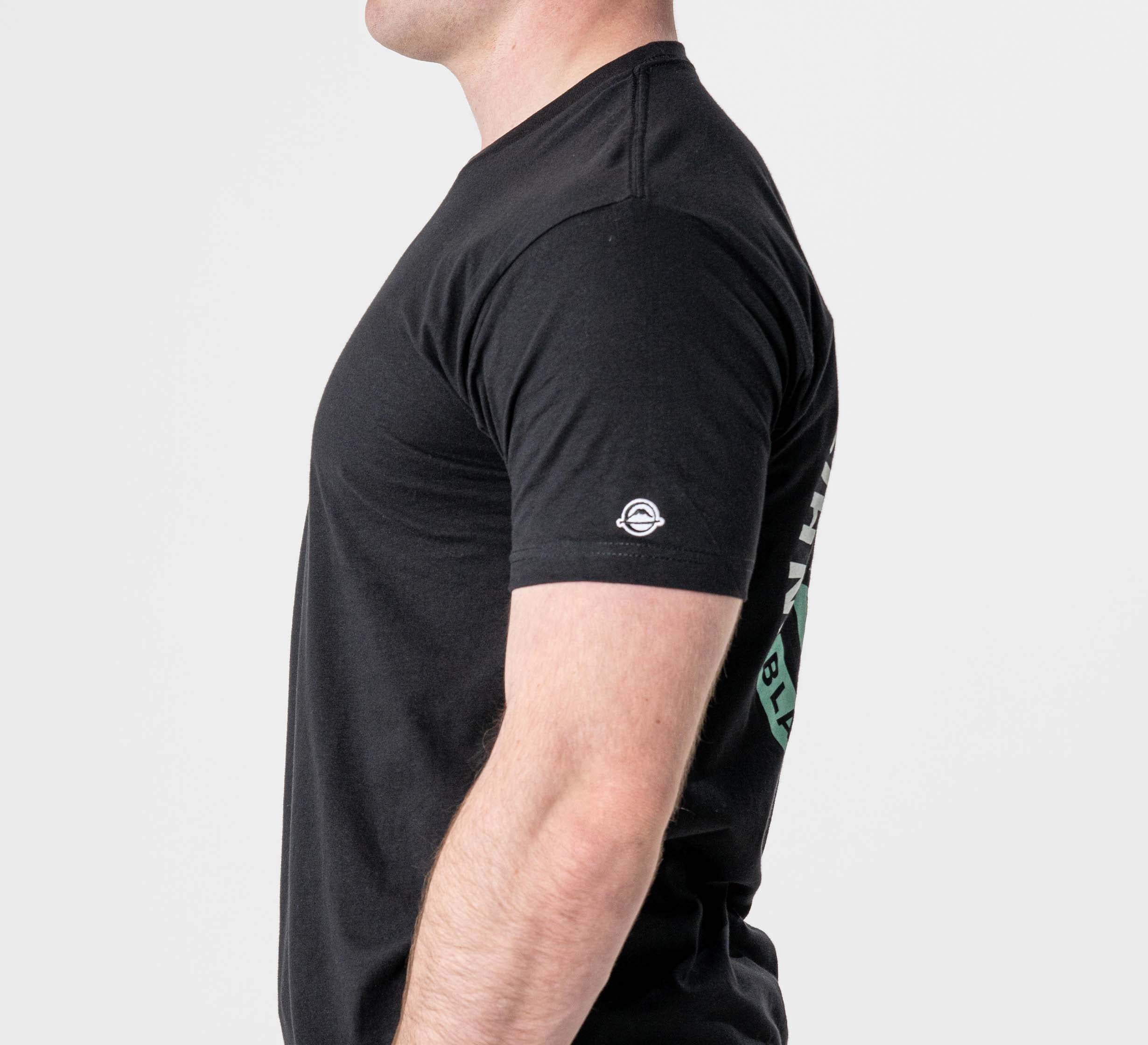 A man is shown in profile against a plain white background wearing the Black Belt Mentality T-Shirt Black, featuring a small white circular logo on the sleeve.