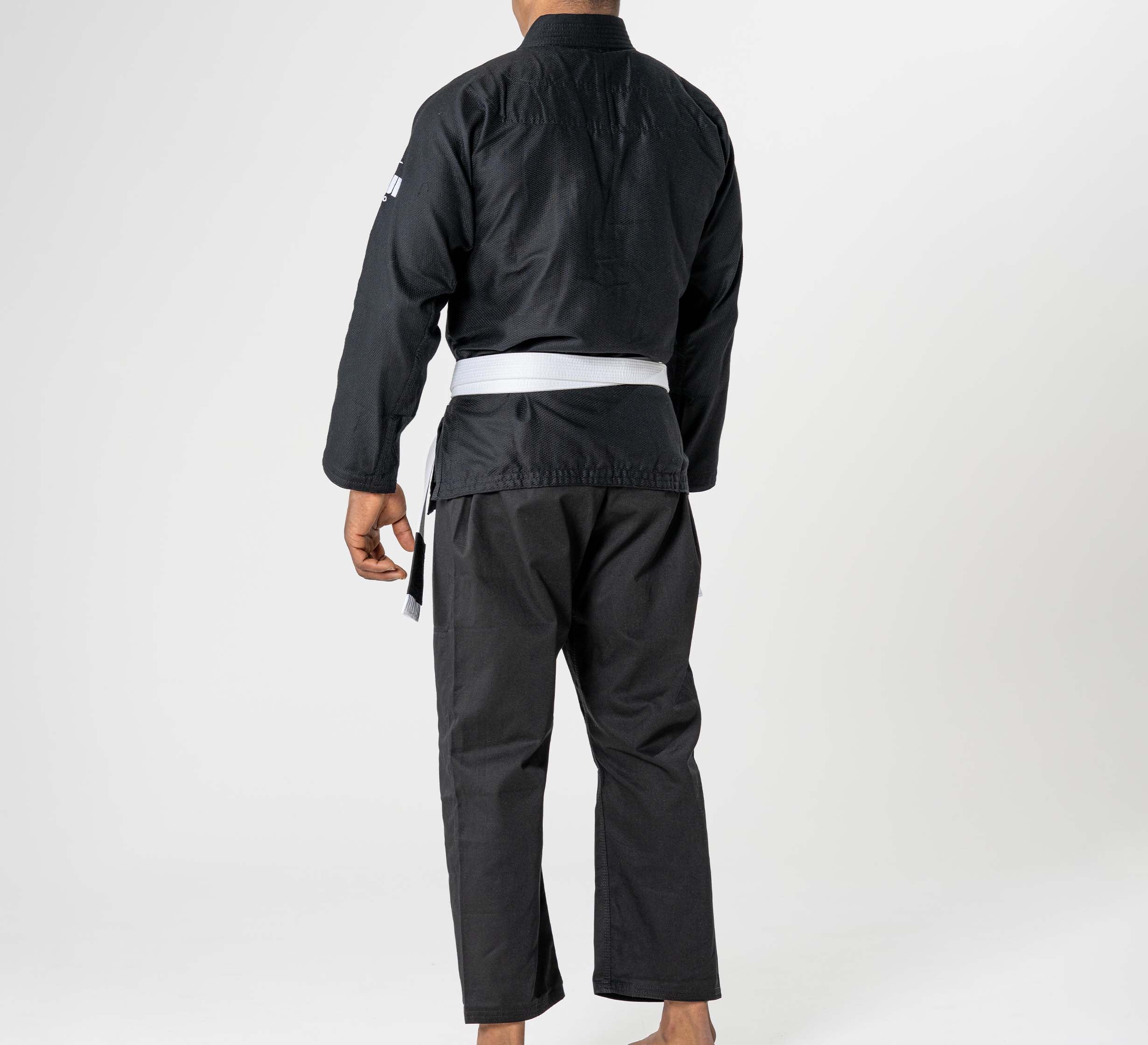A person stands barefoot facing away, wearing the Starter Adult BJJ Gi Black with a white belt, against a plain white background.
