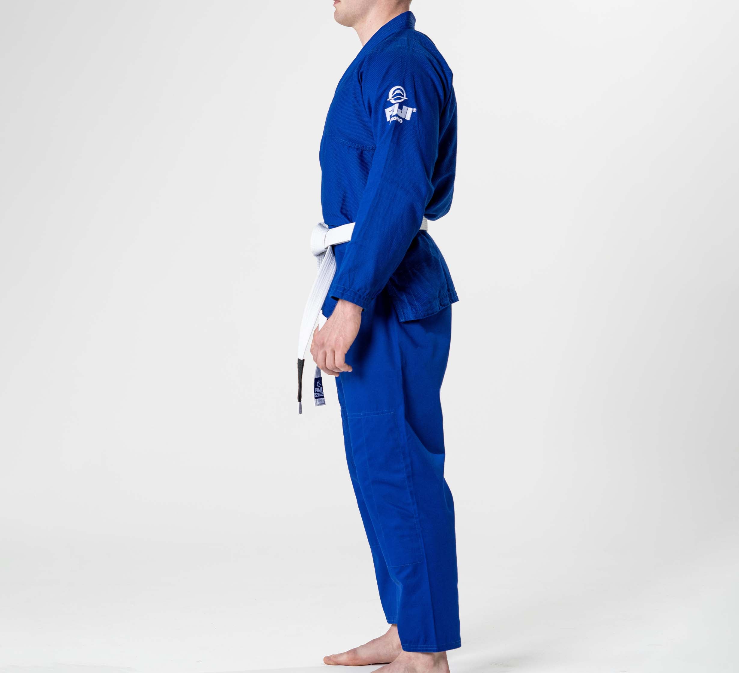 A person wearing the Starter Adult BJJ Gi Blue with a white belt stands barefoot in side profile against a plain white background.