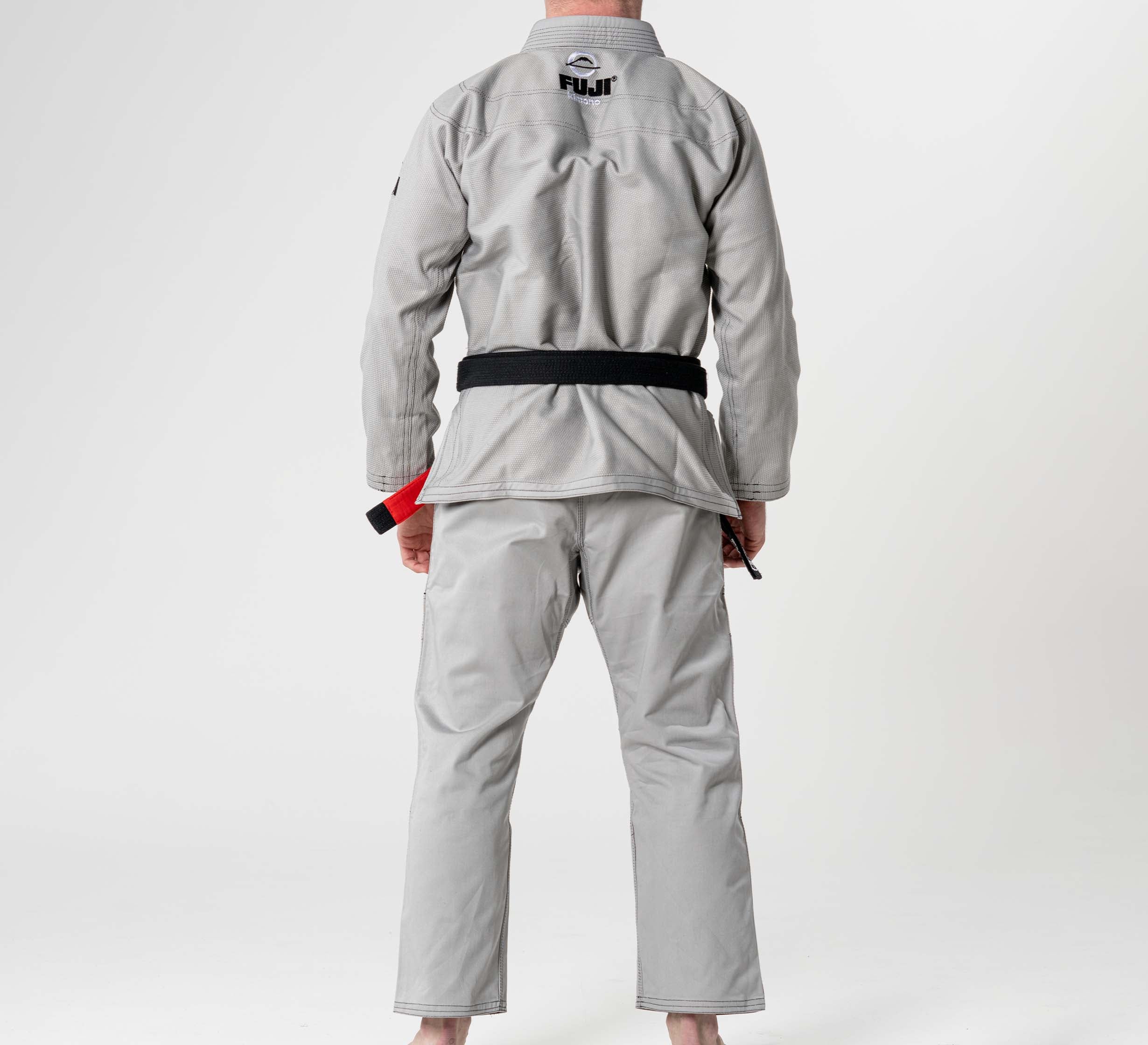 A person in a Lightweight BJJ Gi Grey with a black belt stands barefoot, facing away on a white background. The back of the gi displays the FUJI brand logo.