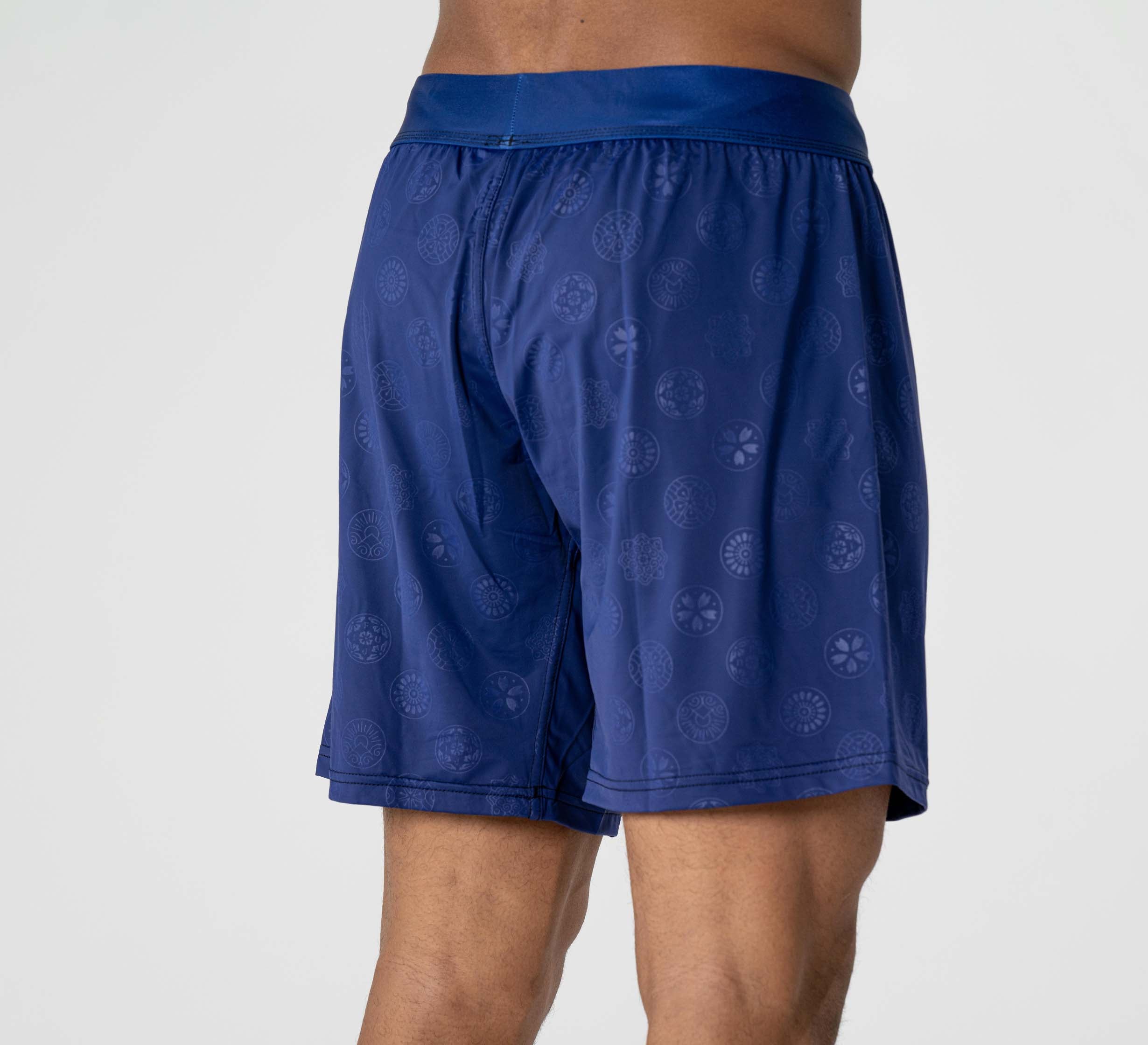 A person models the Shogun Heat Gear Shorts in navy, featuring a subtle circular pattern, standing with back and partial side view against a plain light background.