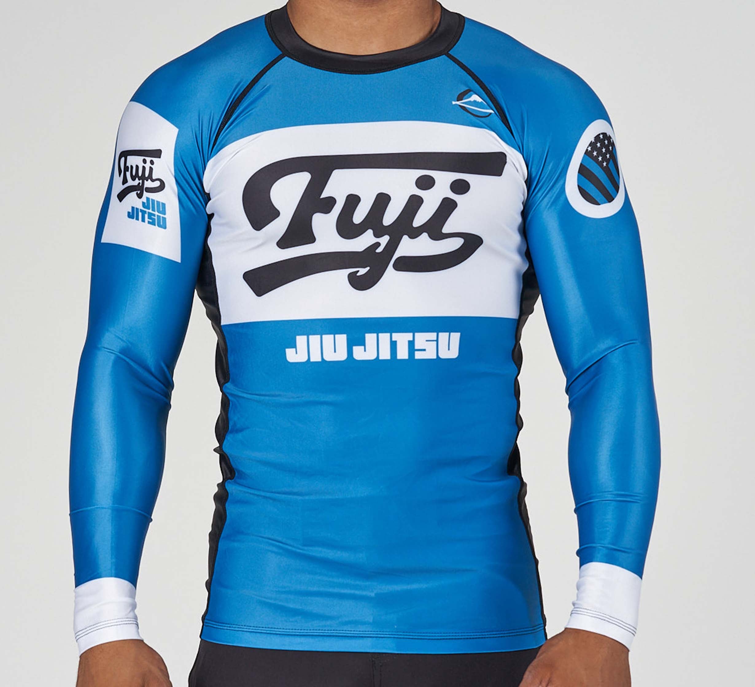 A person wearing the Jiu Jitsu Script Flex Lite Long Sleeve Rashguard Blue, featuring Fuji and JIU JITSU printed on the front, with Fuji and flag patches on the sleeves.