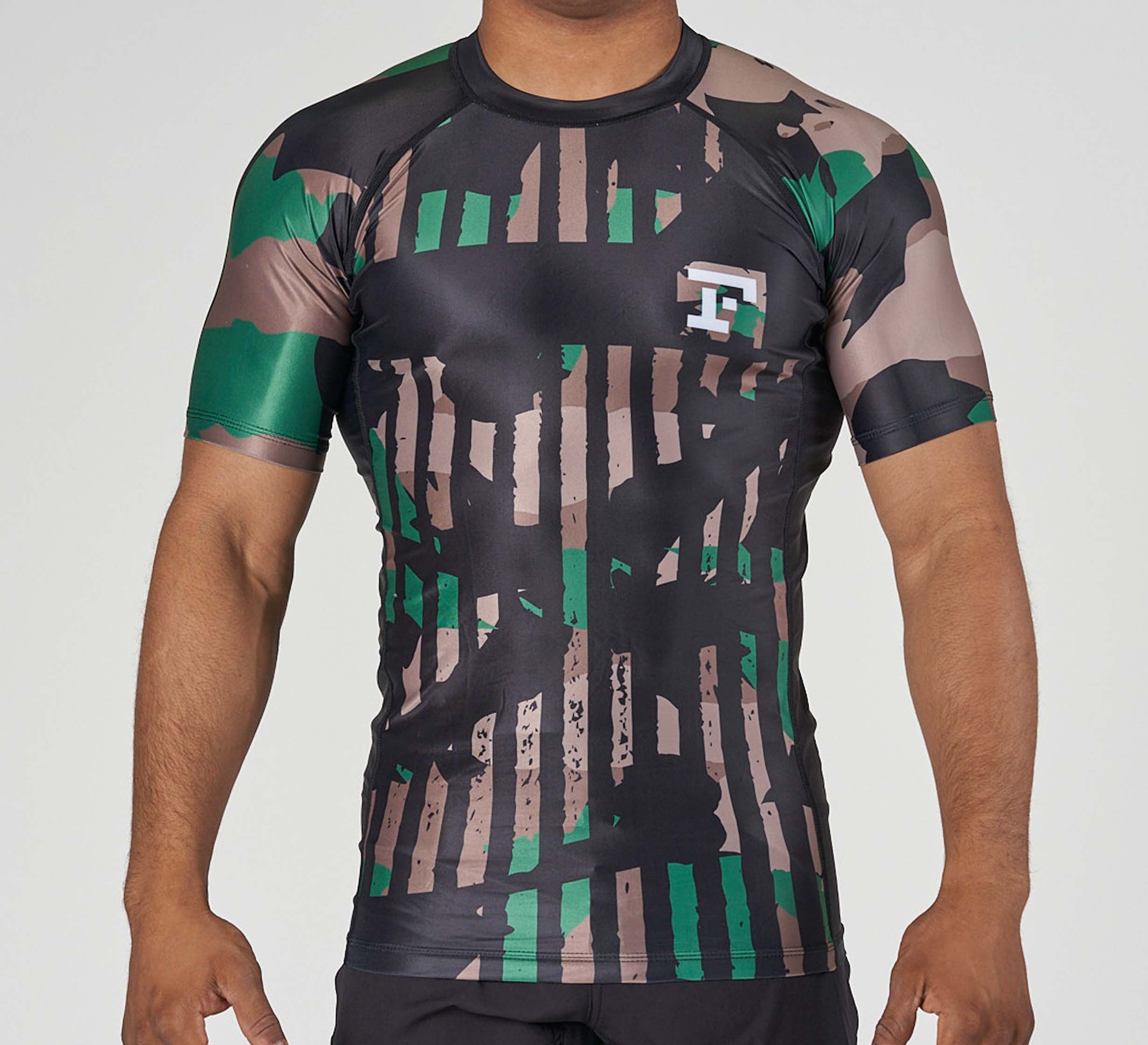A person wearing the Camo Flex Lite Rashguard—a fitted, short-sleeve athletic shirt with green, brown, and black camouflage stripes and a small white and green logo on the left chest. Only the upper body is shown.