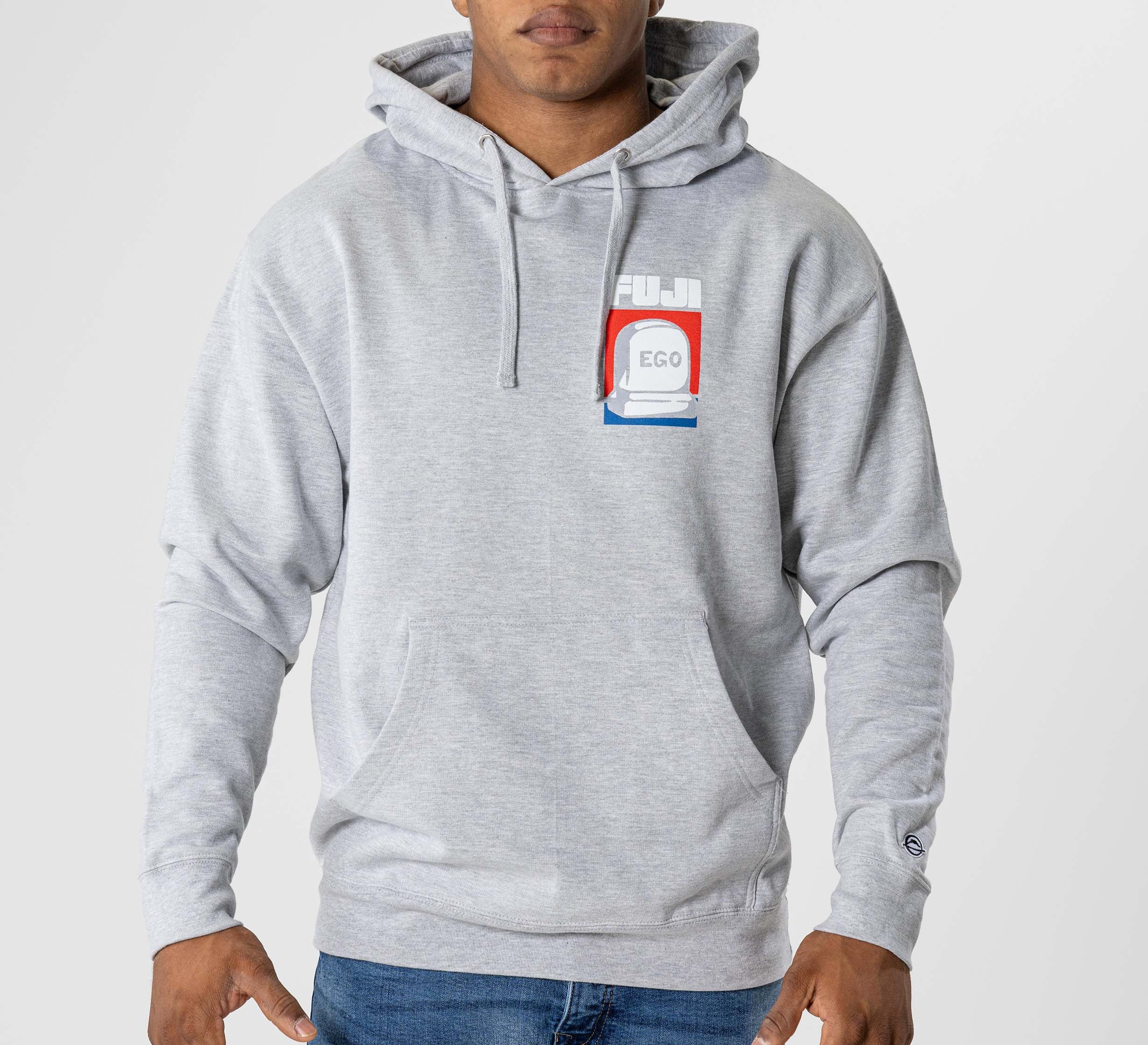 A person wearing the Submit Your Ego Hoodie in heather grey, featuring a front pocket and a small, colorful cassette tape graphic with "FUJI" and "EGO" on the left chest, stands against a plain background.