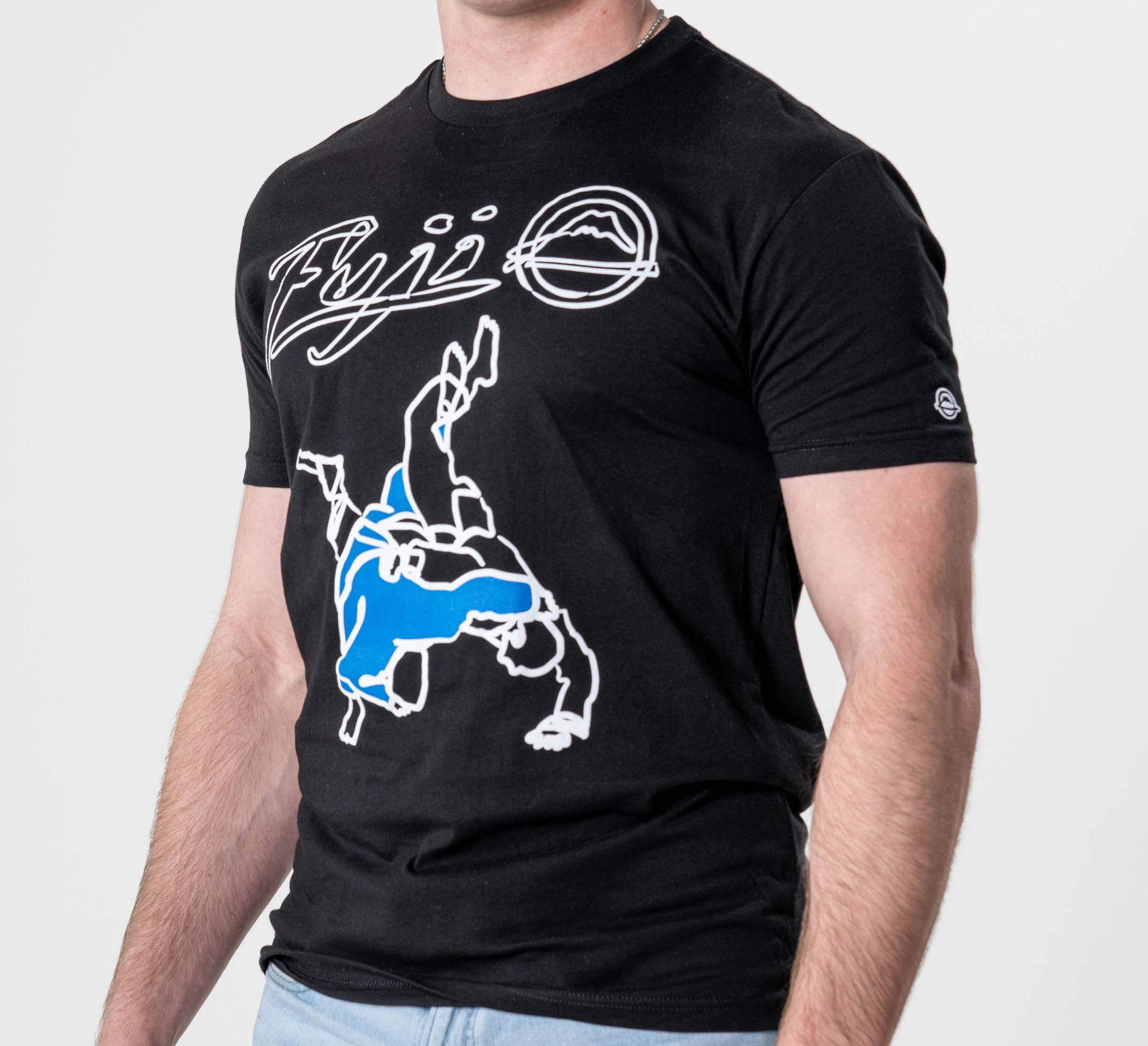 Someone wearing the FUJI Takedown T-Shirt Black, featuring "Fiji" and a mountain logo in white with a bold blue and white upside-down figure graphic, paired with light blue jeans.