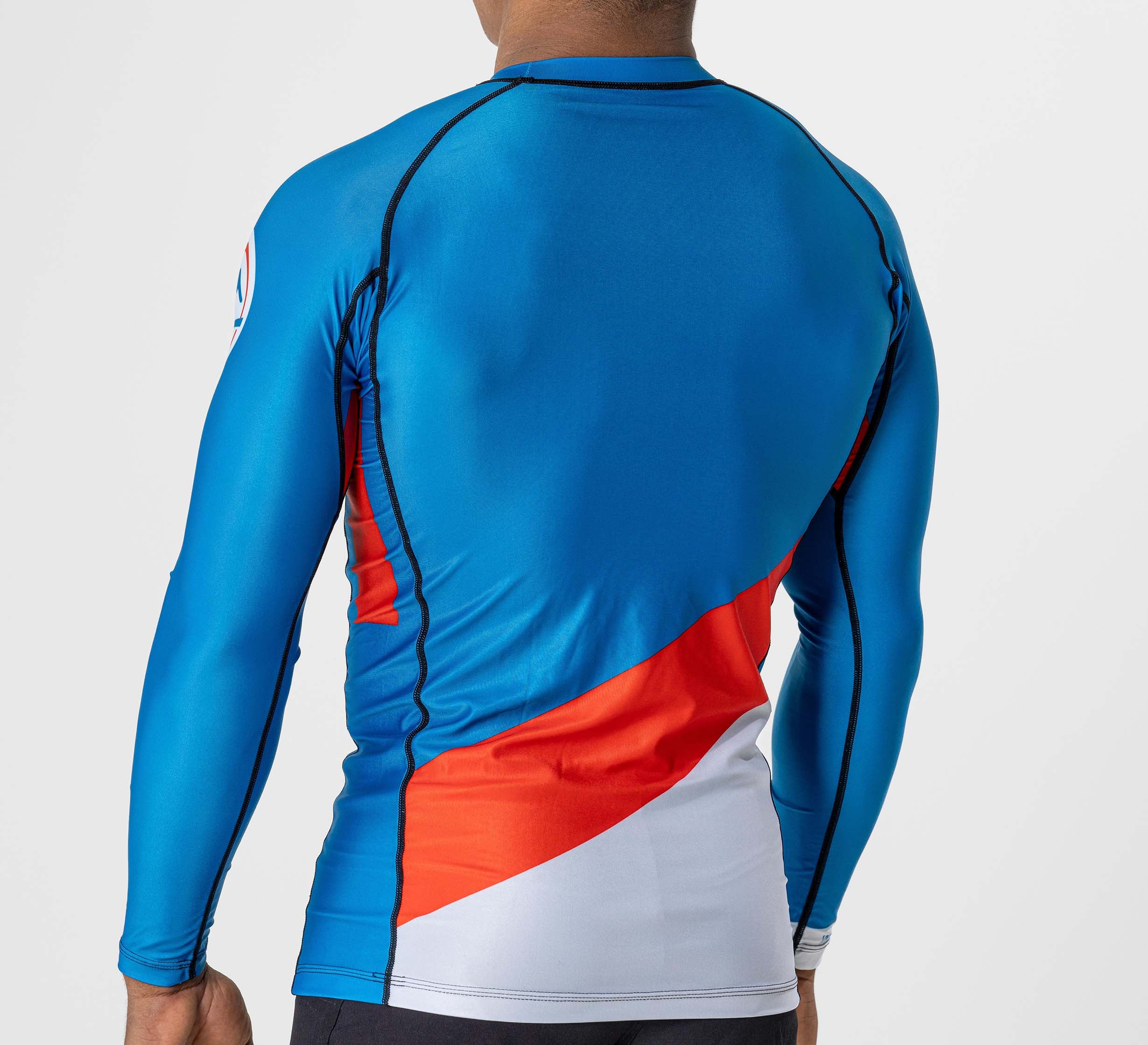 A person is seen from the back wearing the Pacer Flex Lite Long Sleeve Rashguard Blue/Red, standing against a plain light background.