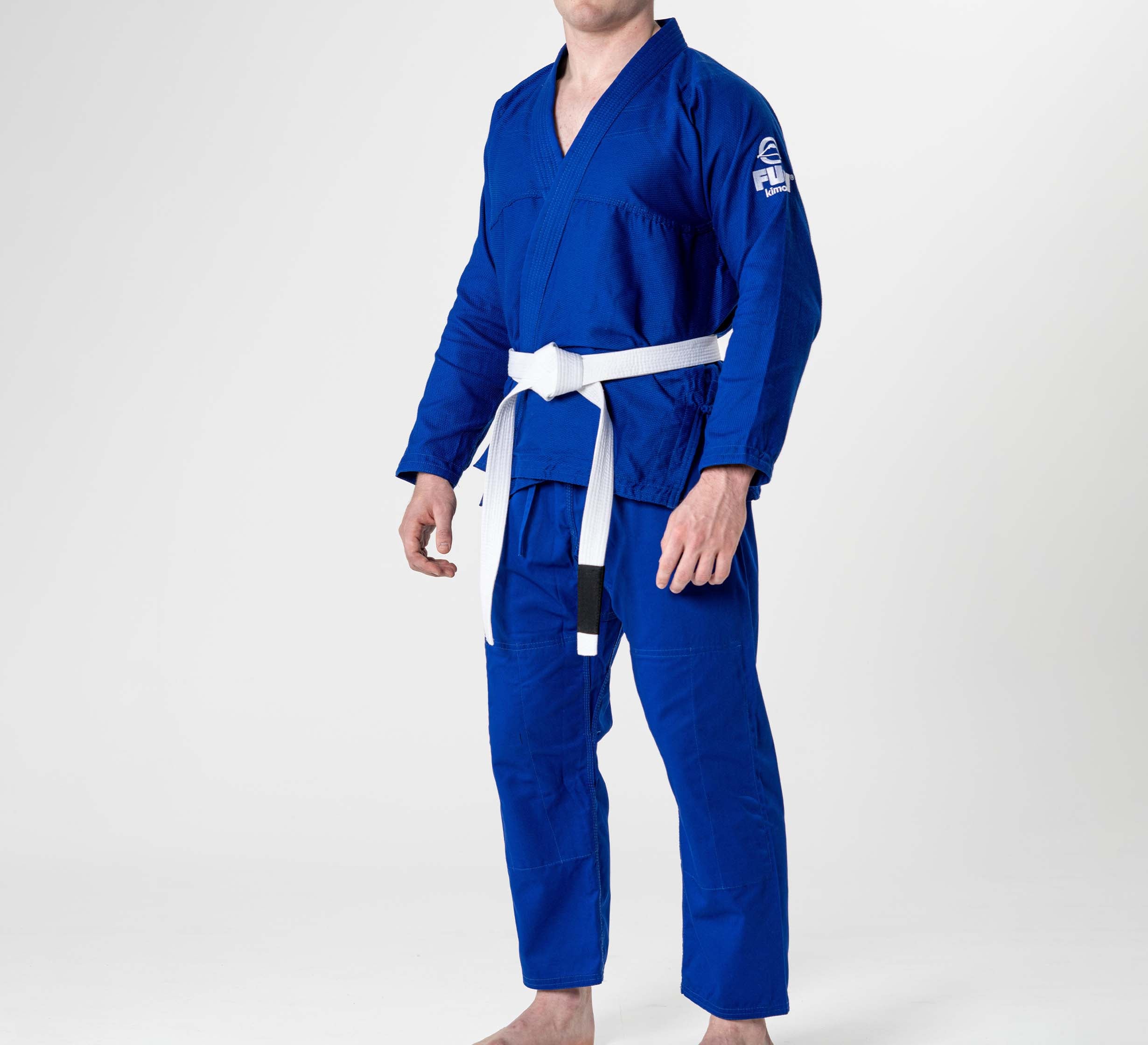 A person wearing the Starter Adult BJJ Gi Blue with a white belt stands barefoot against a plain white background.