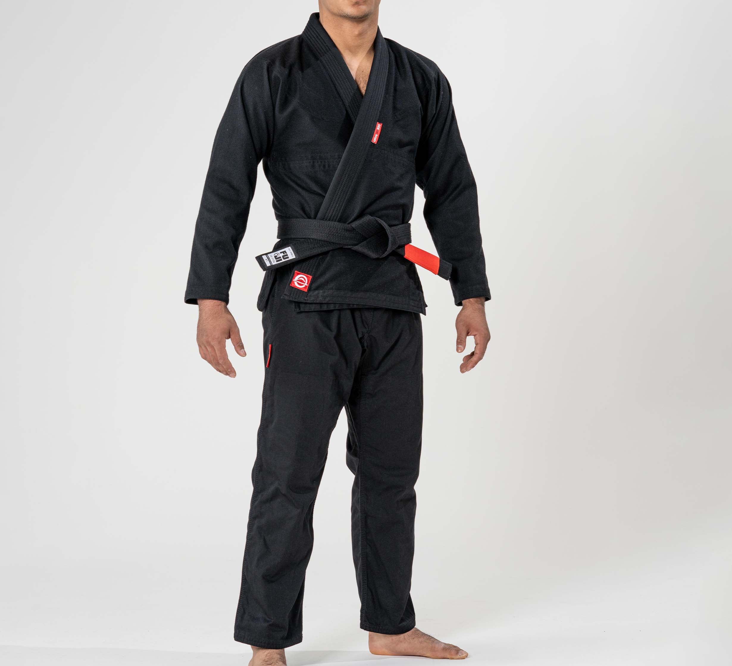 A child stands barefoot in the Kids Ultra Lite 300 BJJ Gi Black with red logos and a black belt featuring a red bar, posed against a plain white background.