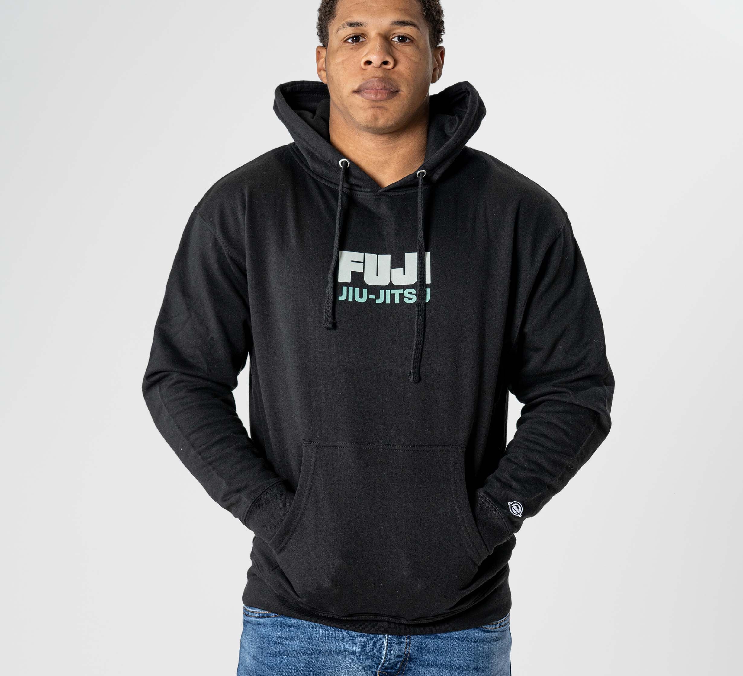Someone wearing the Black Belt Mentality Hoodie Black with hands in the front pocket, standing against a plain light background.