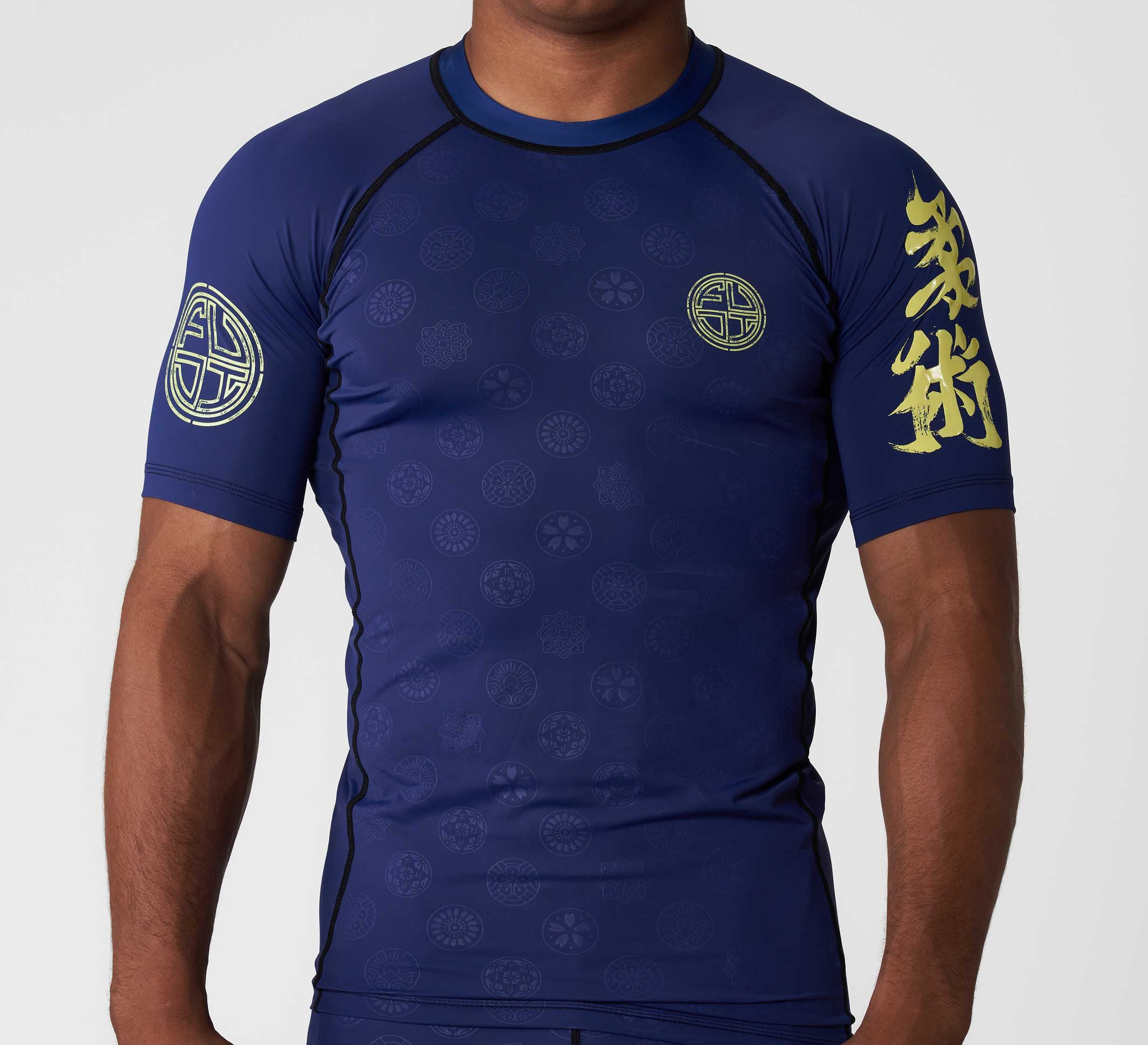 A person wears the Shogun Heat Gear Rashguard Navy, featuring yellow Asian-style symbols on the left sleeve and chest with subtle circular patterns. The individual's head is not visible.