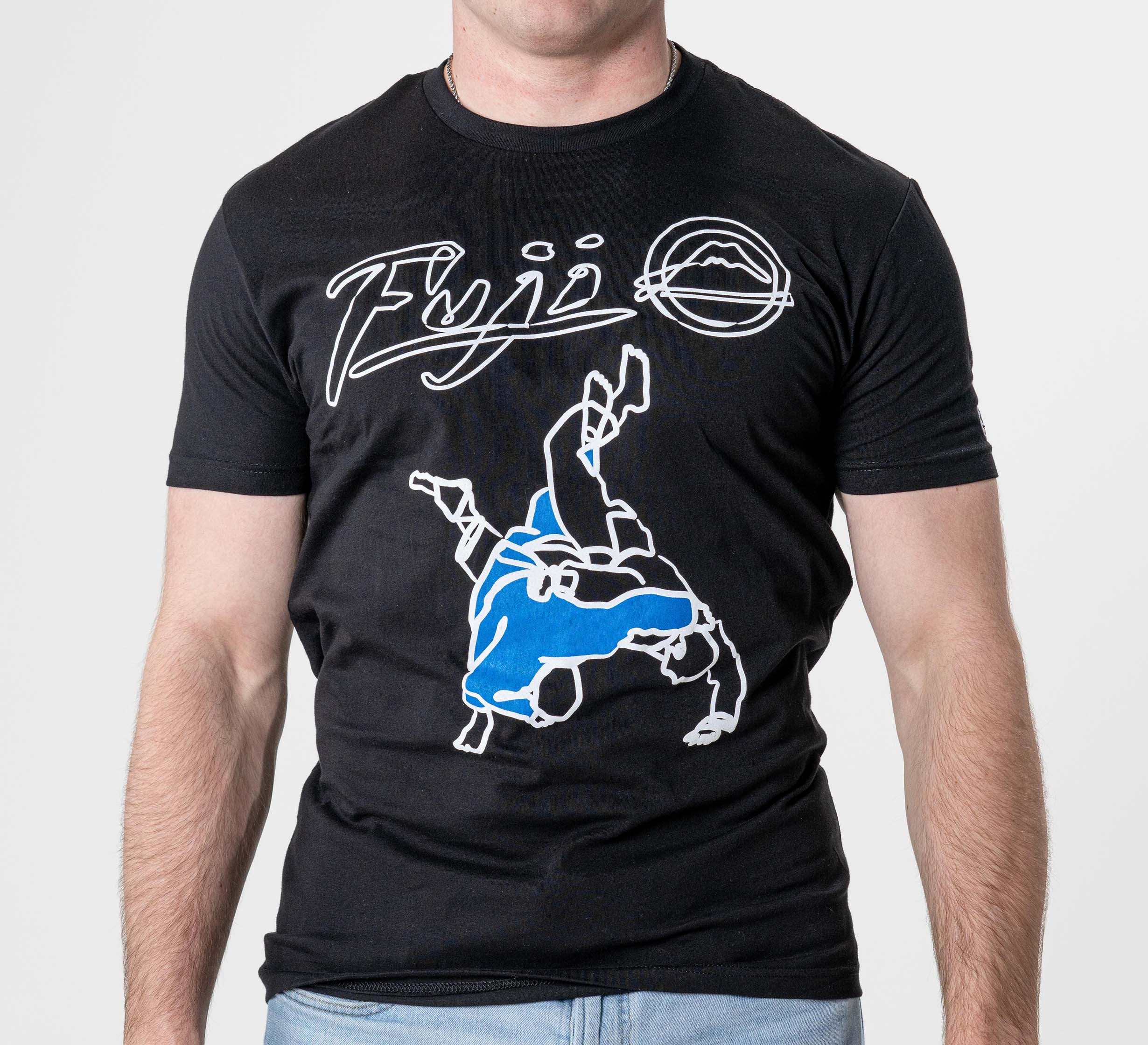 A man wears the FUJI Takedown T-Shirt Black, which features "Fuji," a graphic of two people grappling with one flipping the other, white and blue accents, and a stylized mountain logo.