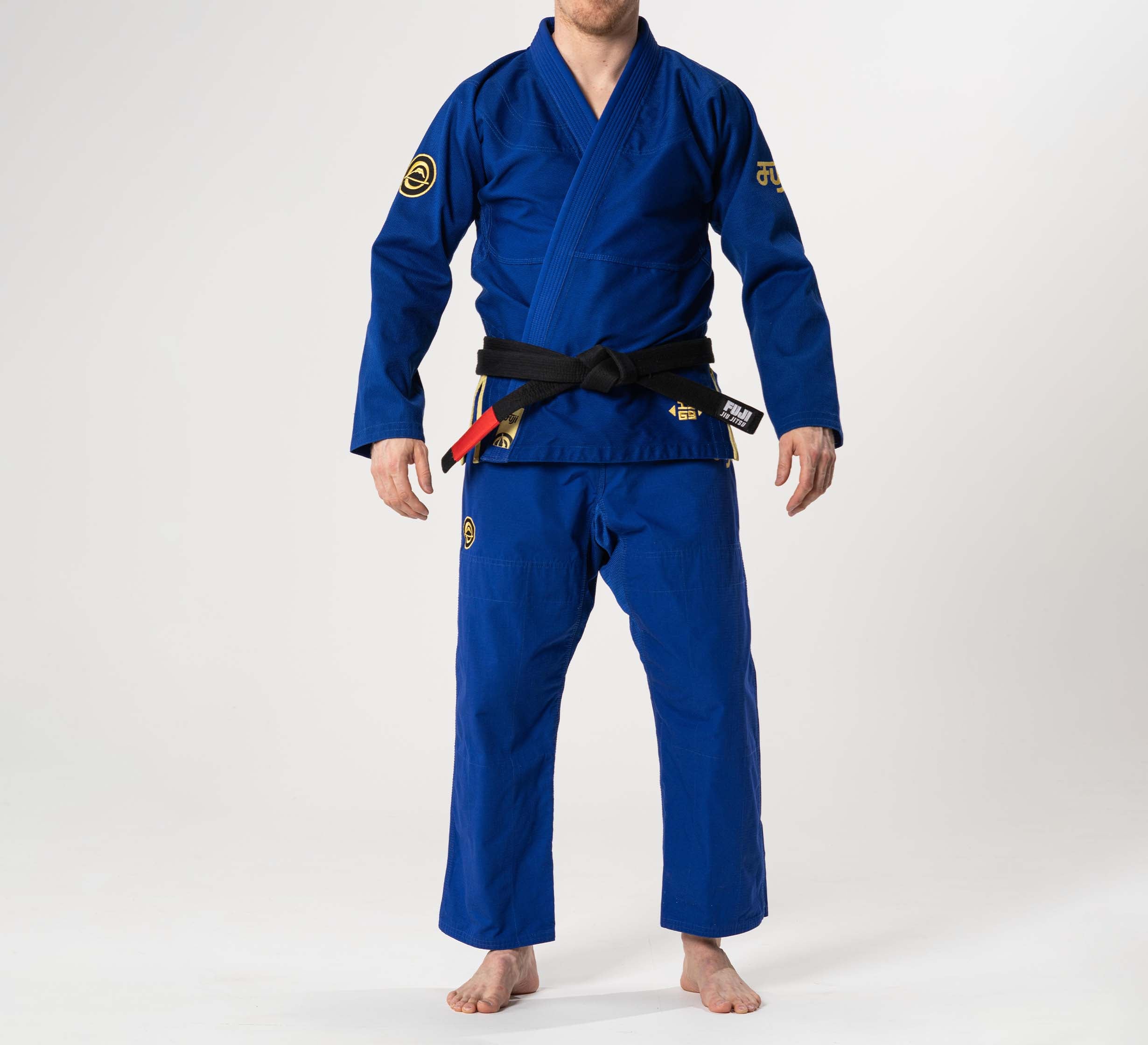 A person wearing the Flow-Tech BJJ Gi Blue/Gold with a black belt stands barefoot against a plain white background. Their head is not fully visible.