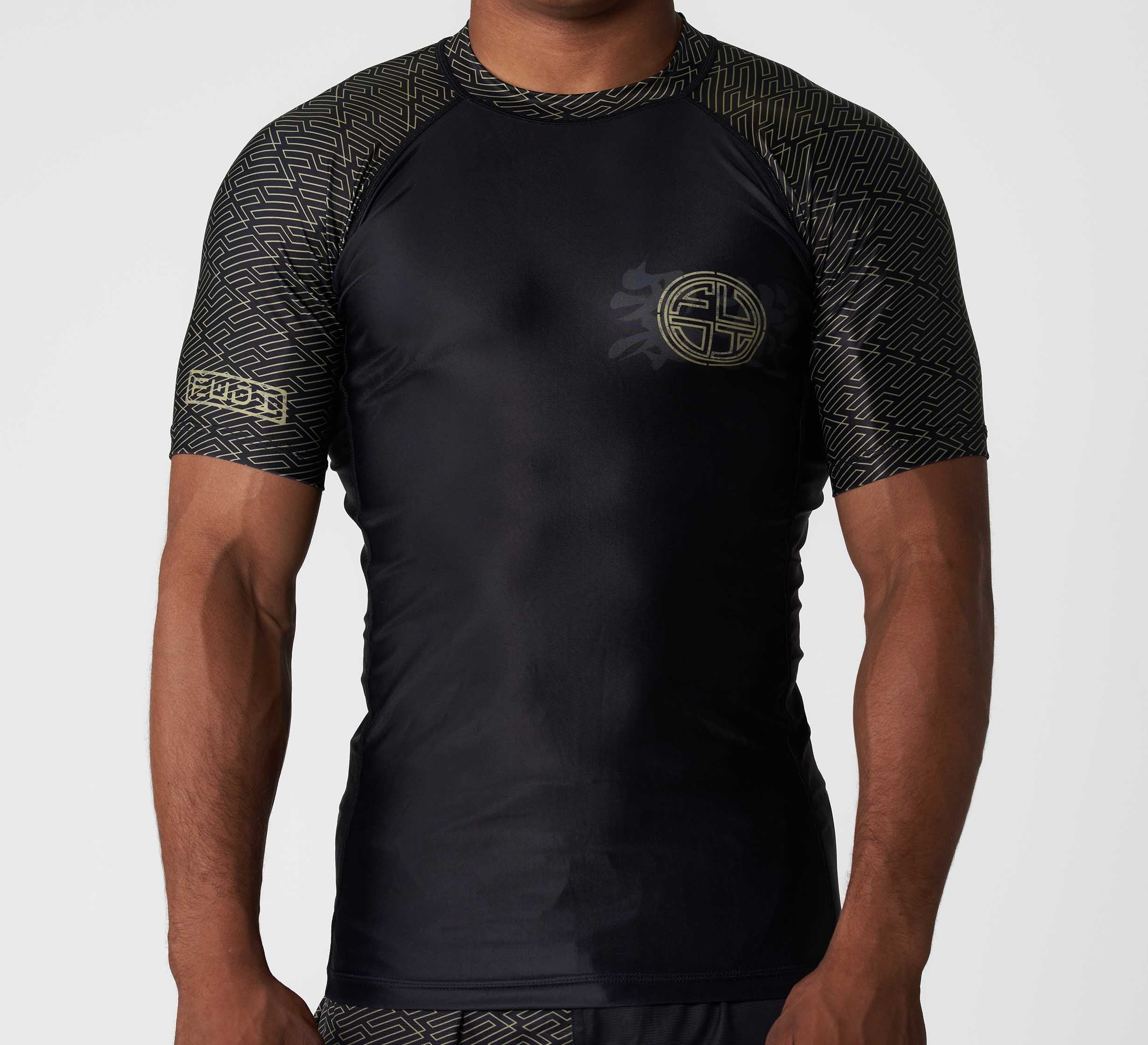 A man wears the Bushido Flex Lite Rashguard, a fitted short-sleeve black top featuring geometric sleeve and edge patterns and a circular emblem on the left chest, set against a plain white background.