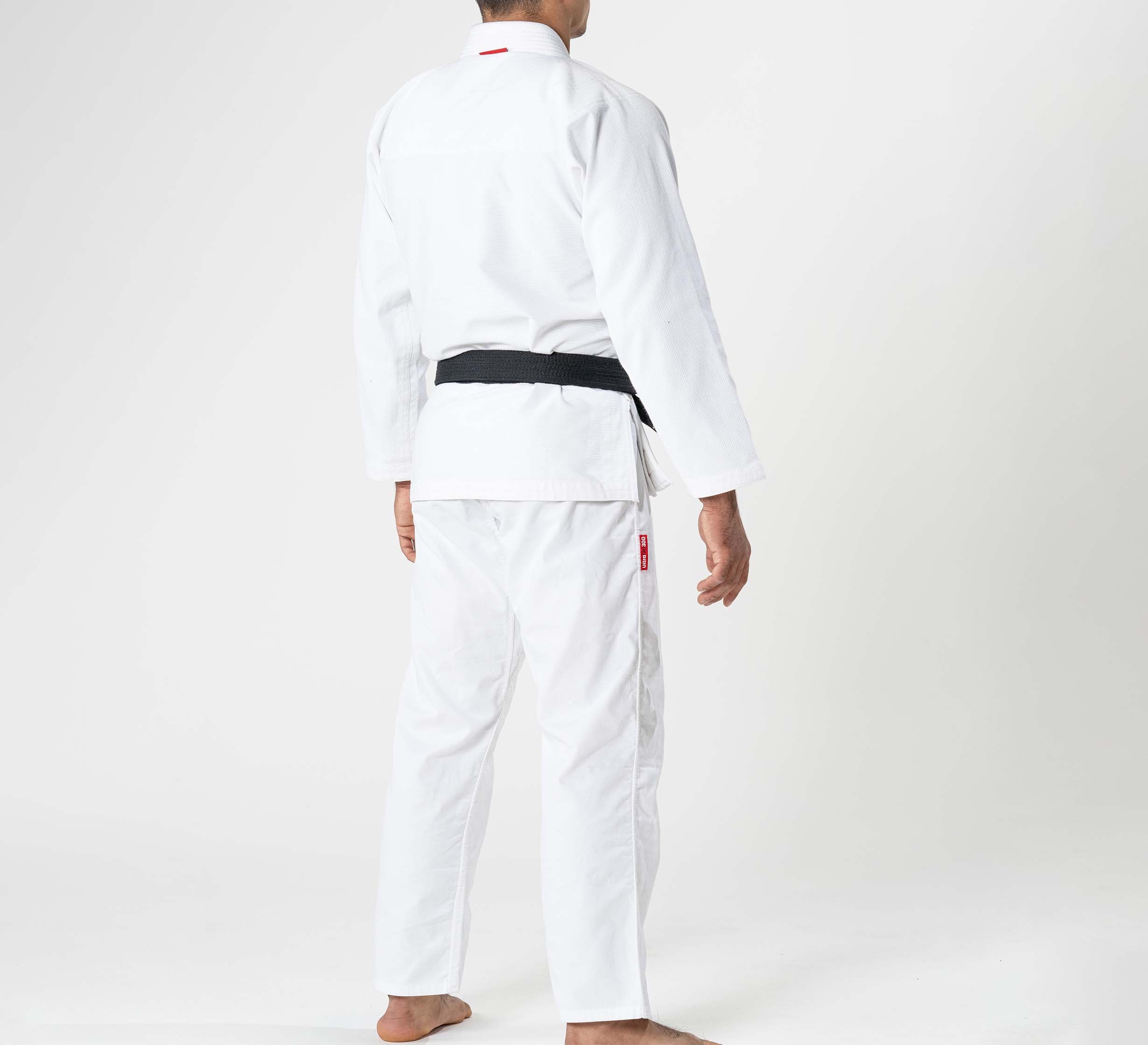 A child in a Kids Ultra Lite 300 BJJ Gi White stands barefoot with their back to the camera, showcasing the martial arts uniform and black belt against a plain white background.