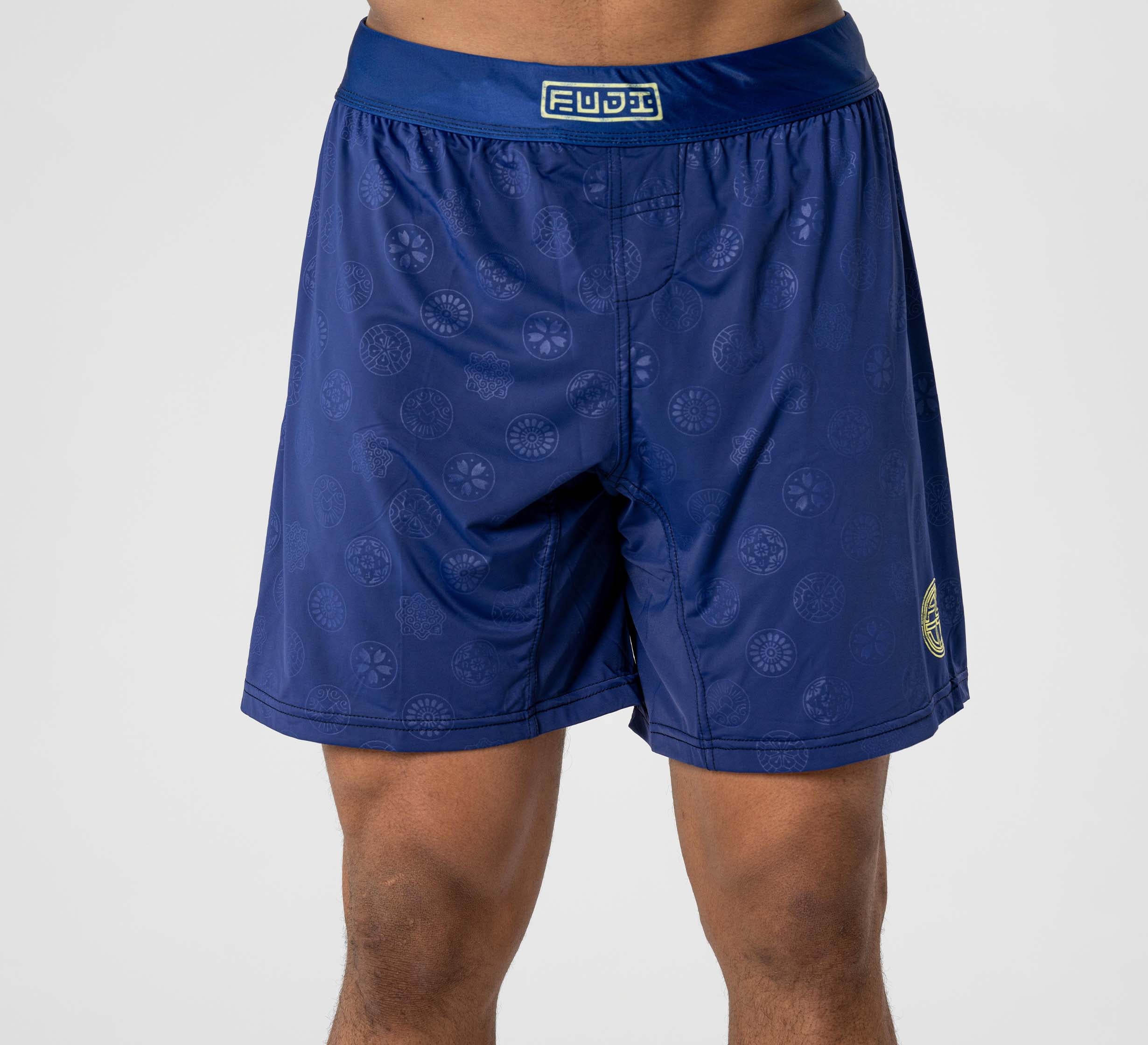 A person wearing Shogun Heat Gear Shorts Navy, featuring a subtle circular pattern and a FUJI logo on the waistband, stands against a plain light background.