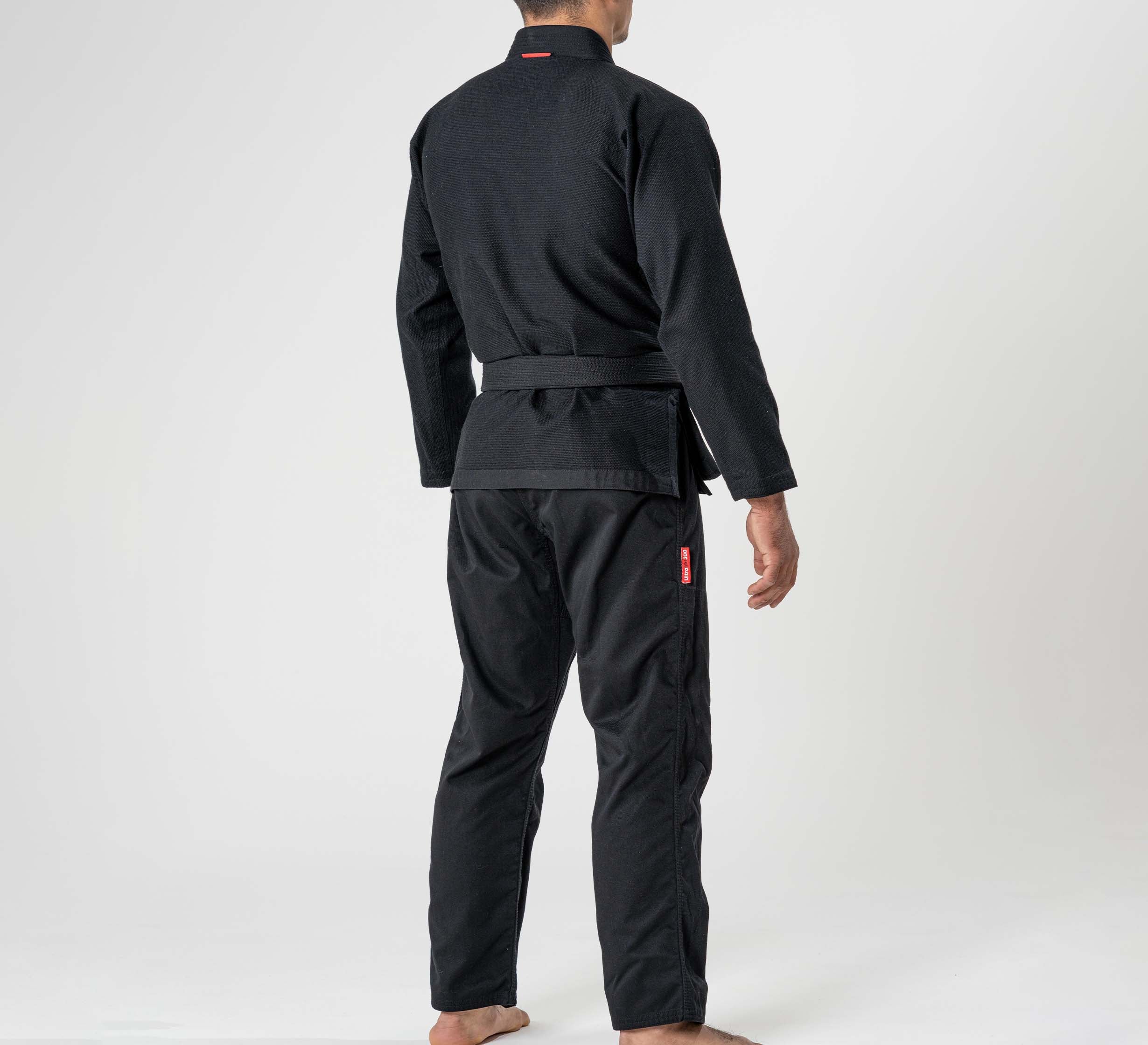 A person stands barefoot on a light background, seen from the back wearing the Ultra Lite 300 BJJ Gi Black with a belt and arms relaxed at their sides.