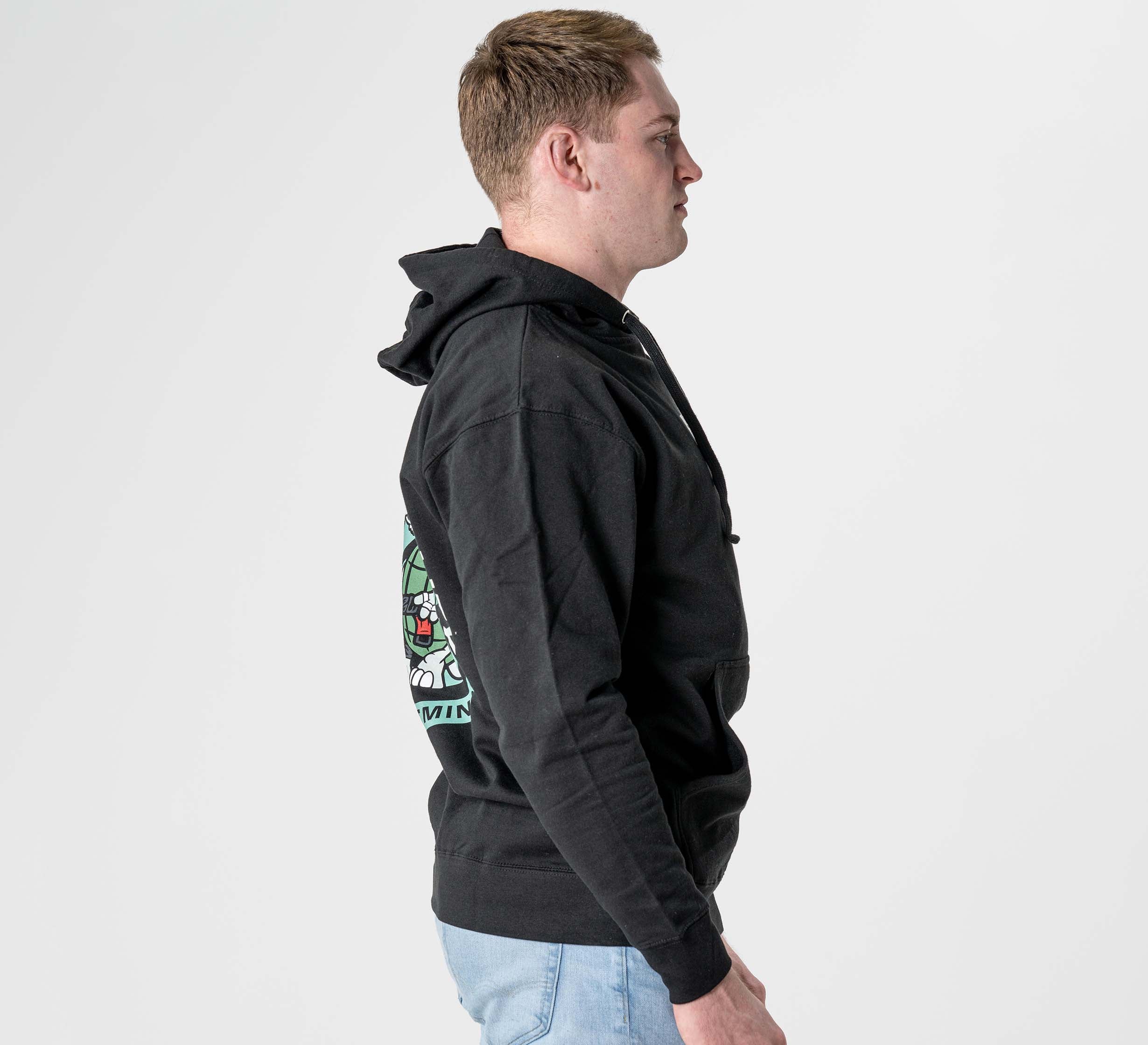 A man stands in profile against a plain white background, wearing the Black Belt Mentality Hoodie Black with a colorful graphic on the back and light blue jeans.