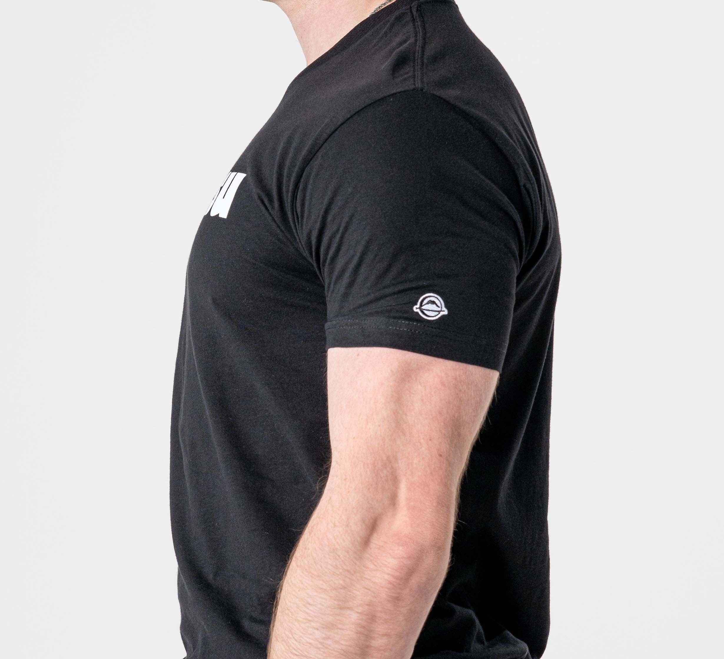 A person shown from the side wears the Jiu Jitsu Player T-Shirt Black, a short-sleeve tee with a small circular logo on the sleeve and partial white text on the chest. The plain white background emphasizes the shirt.