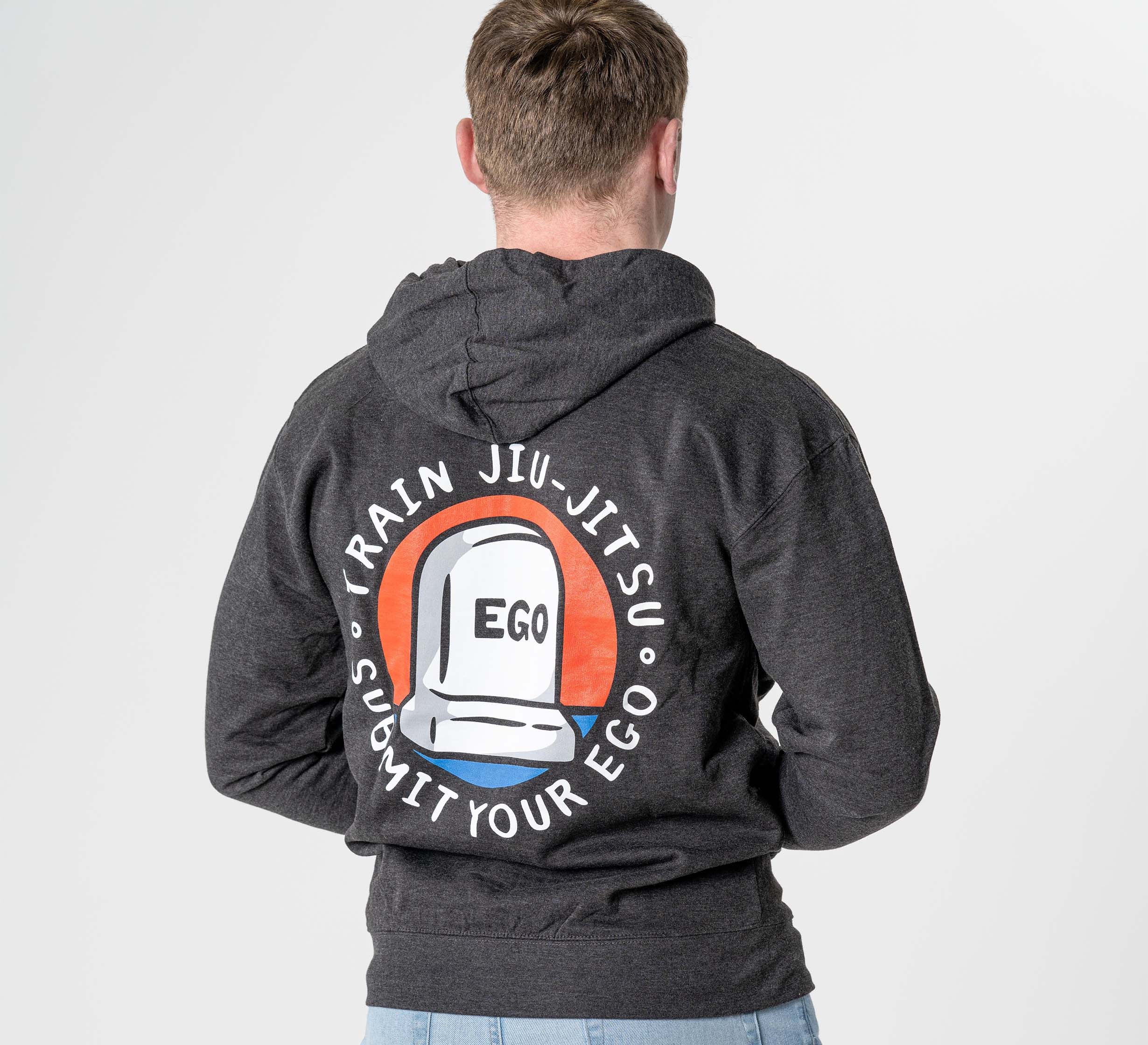A person wearing the Submit Your Ego Hoodie Heather Black, featuring a tombstone graphic labeled "EGO" and the text "TRAIN JIU-JITSU SUBMIT YOUR EGO" on the back, is seen facing away from the camera.
