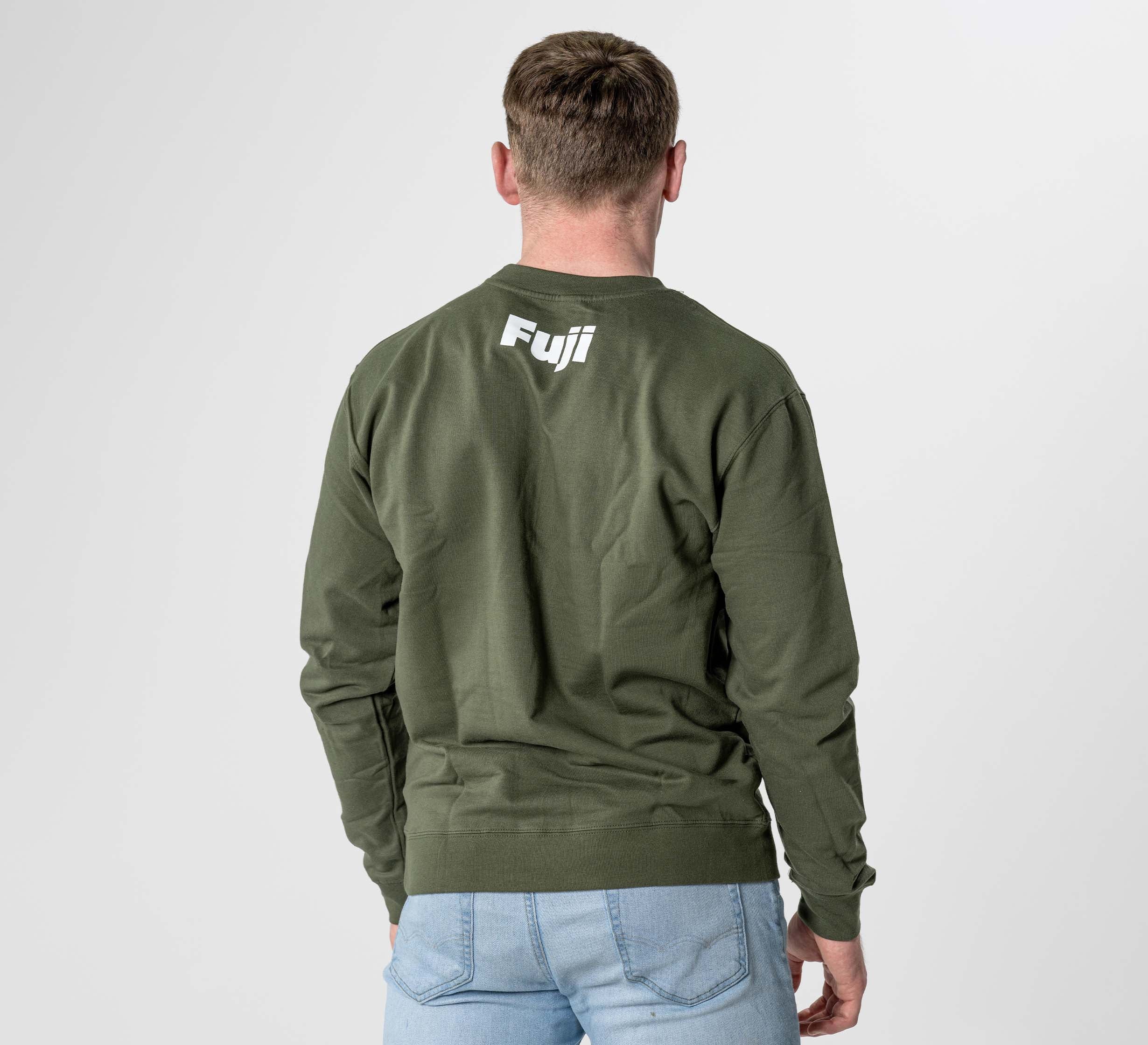A person wearing the Jiu Jitsu Player Crewneck in Military Green, featuring "Fuji" printed in white on the upper back, pairs it with light blue jeans and stands with their back to the camera against a plain background.