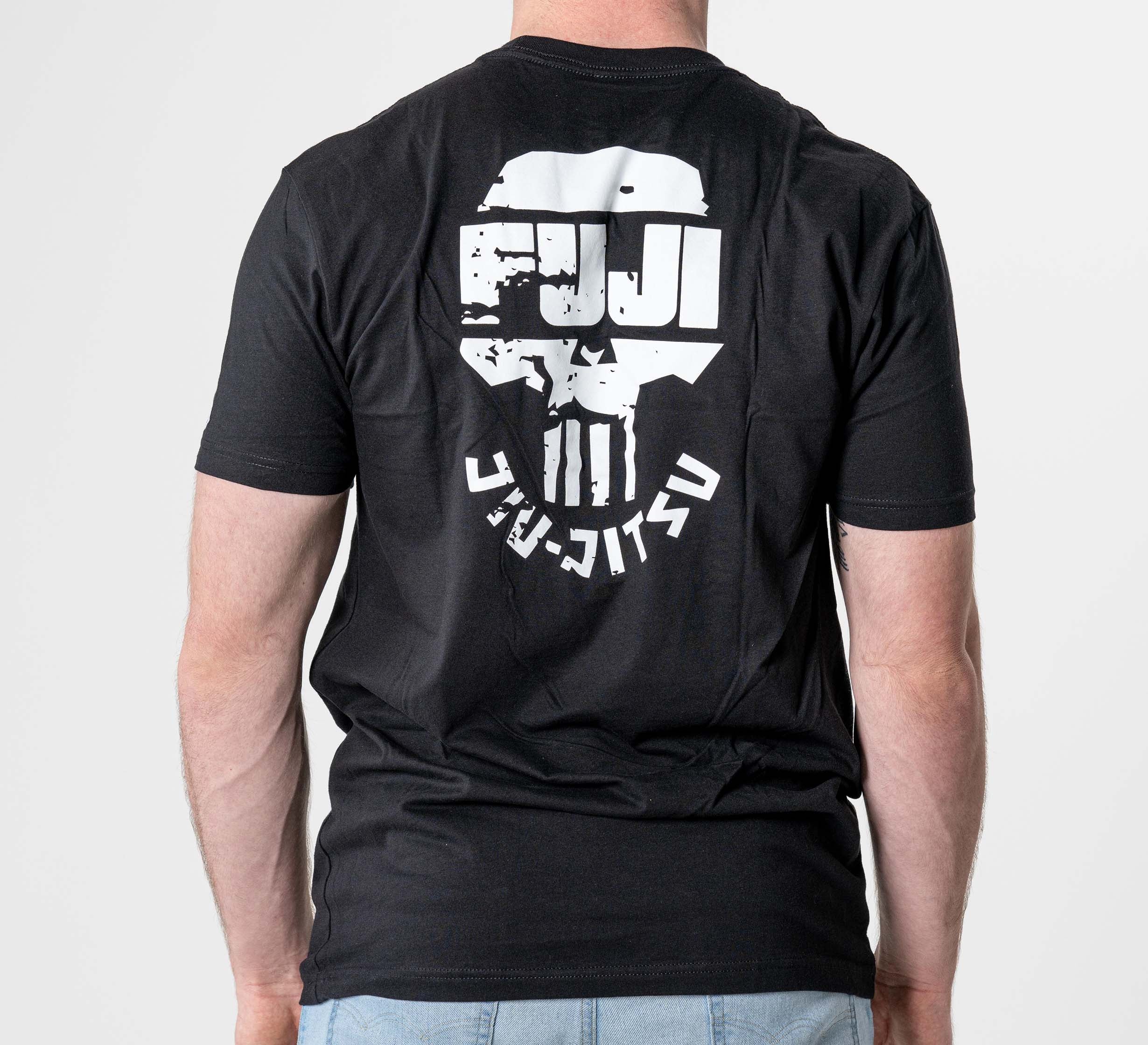 A person is wearing the Punishment T-Shirt Black, featuring a white stylized skull and FUJI Jiu-Jitsu text on the back, standing against a plain light background.
